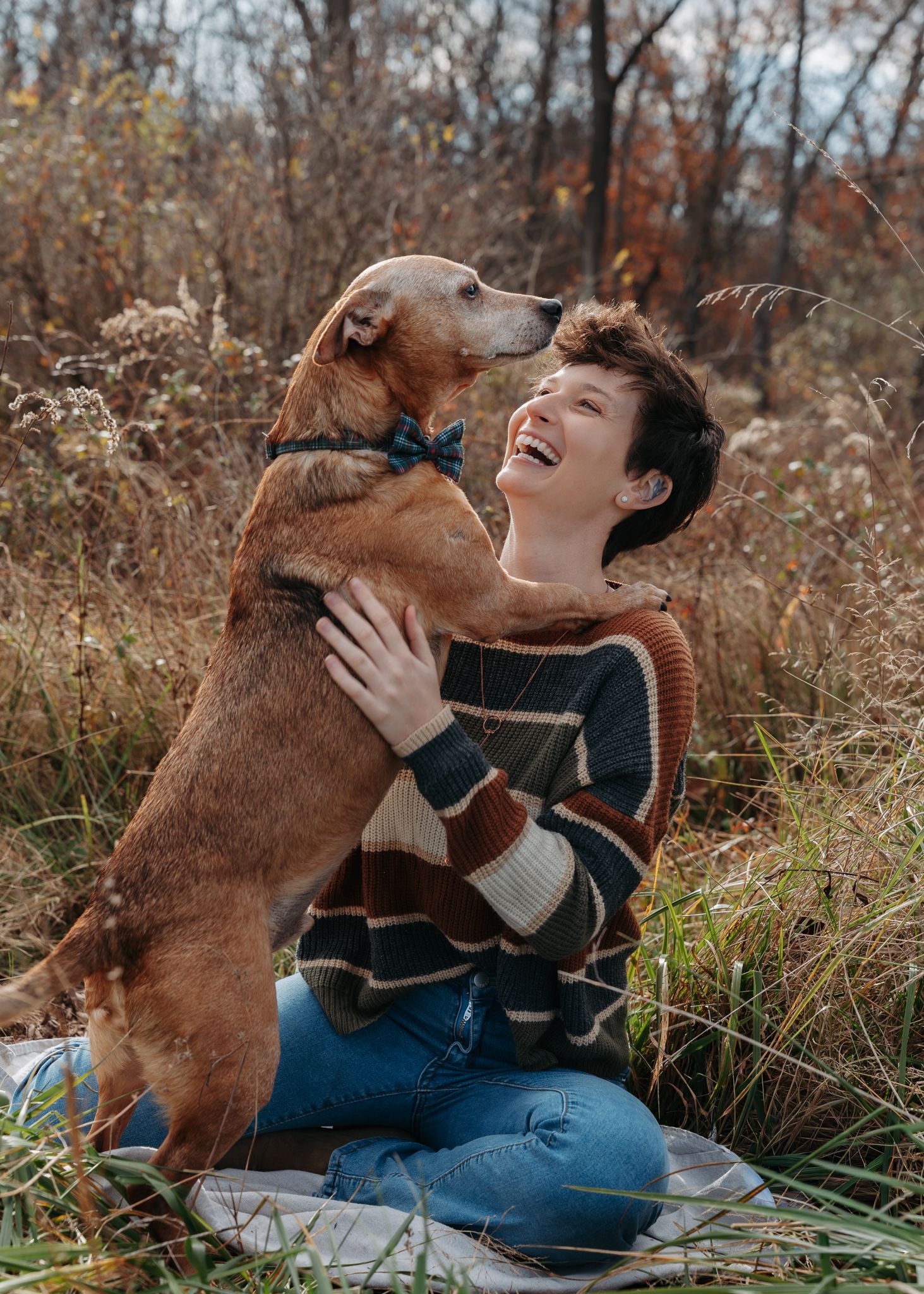 Happy woman laughing outdoors in autumn field while golden retriever dog licks her face.
