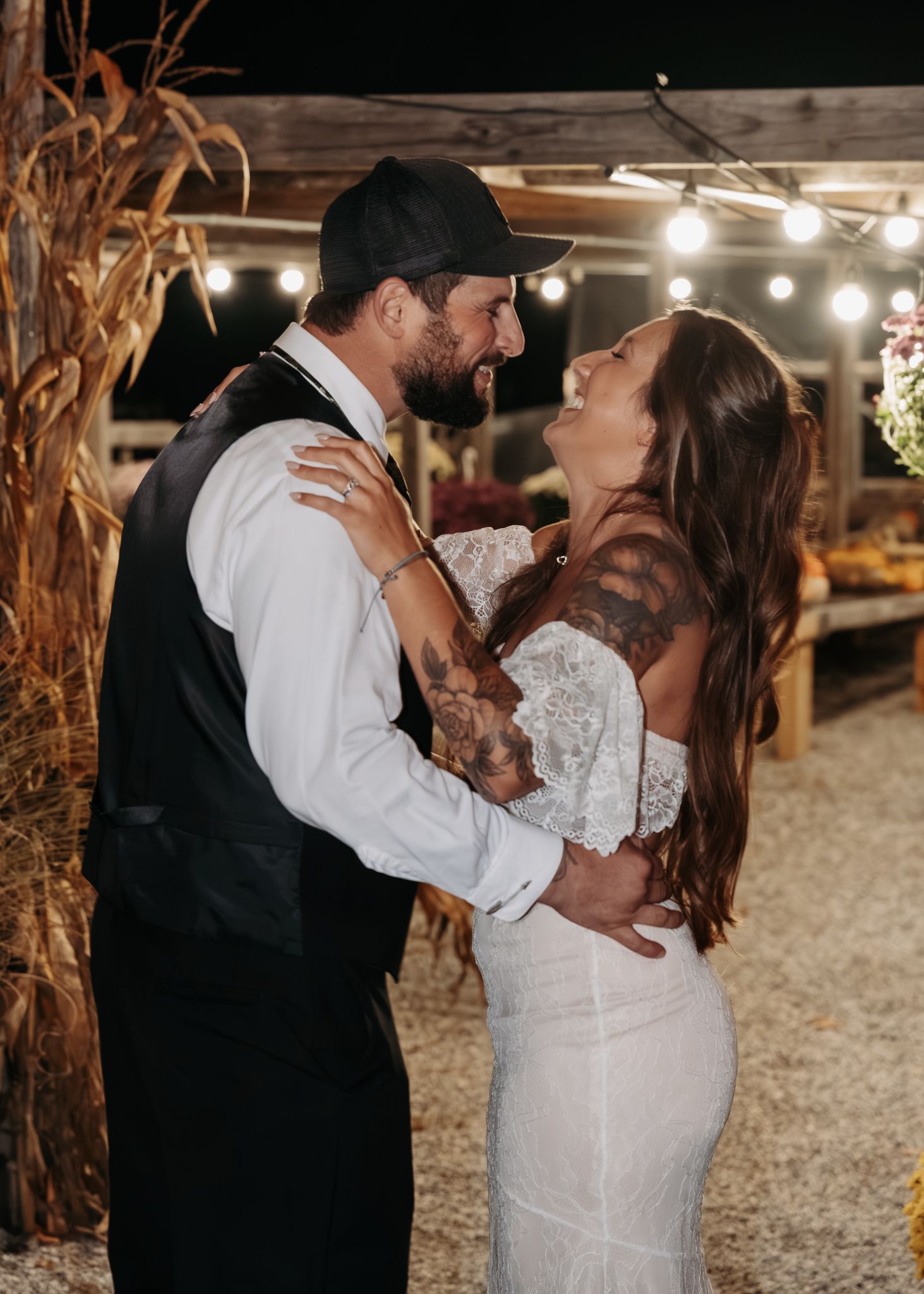 A tattooed couple shares an intimate moment during their first dance under string lights at a rustic outdoor wedding.