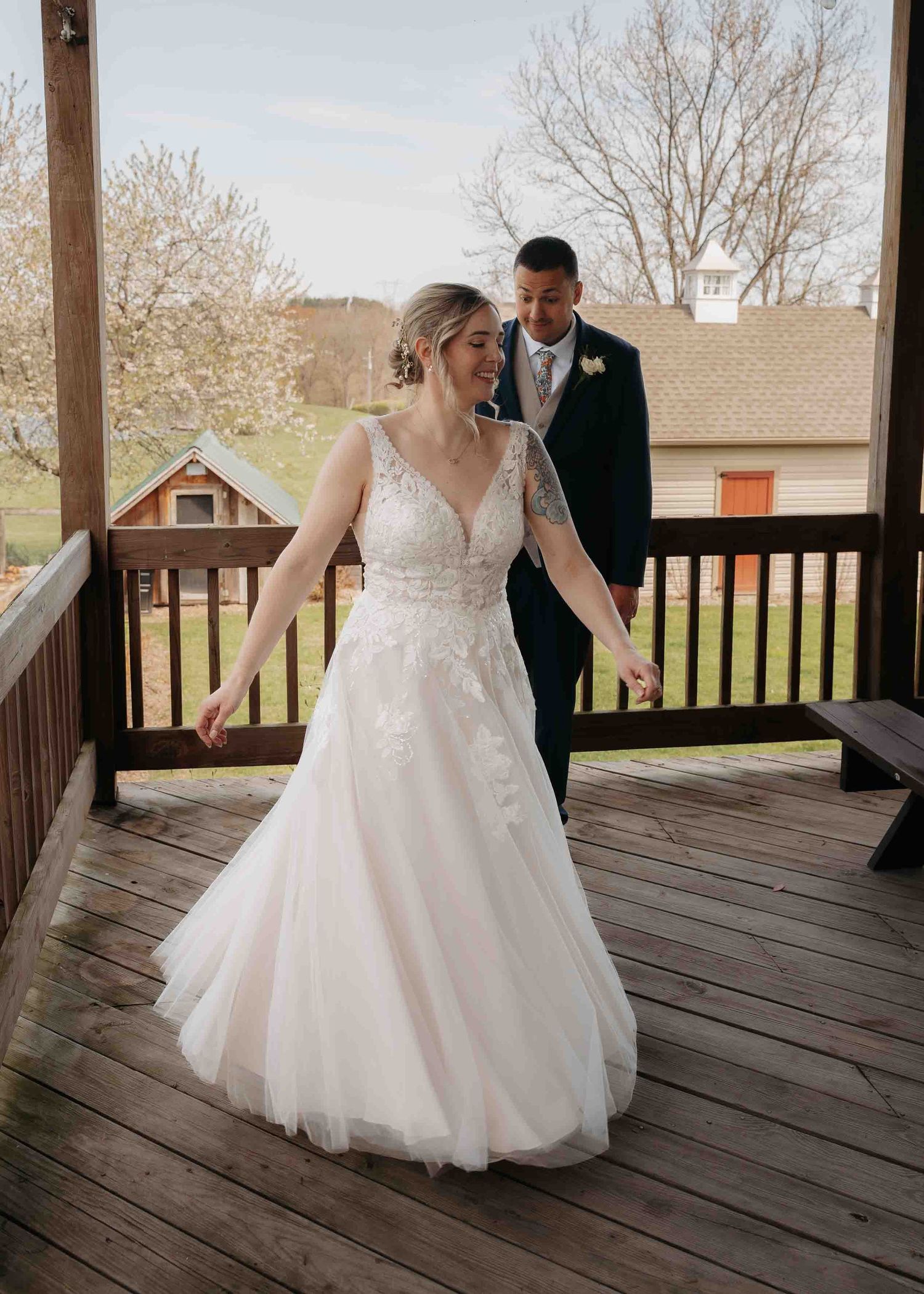 Bride in elegant lace A-line gown shares a first look moment with groom on rustic wooden porch.