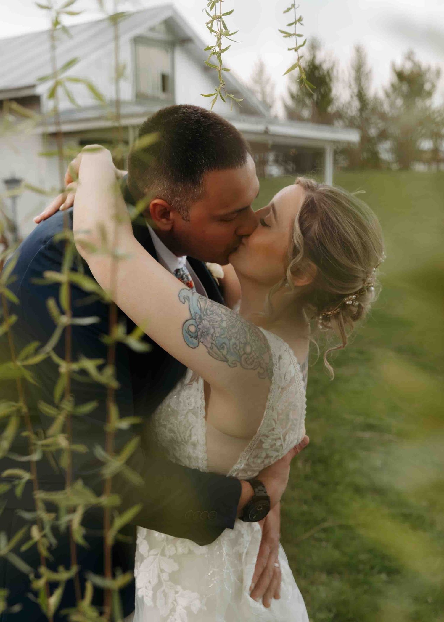 Bride and groom sharing passionate kiss outdoors with lush greenery at wedding.