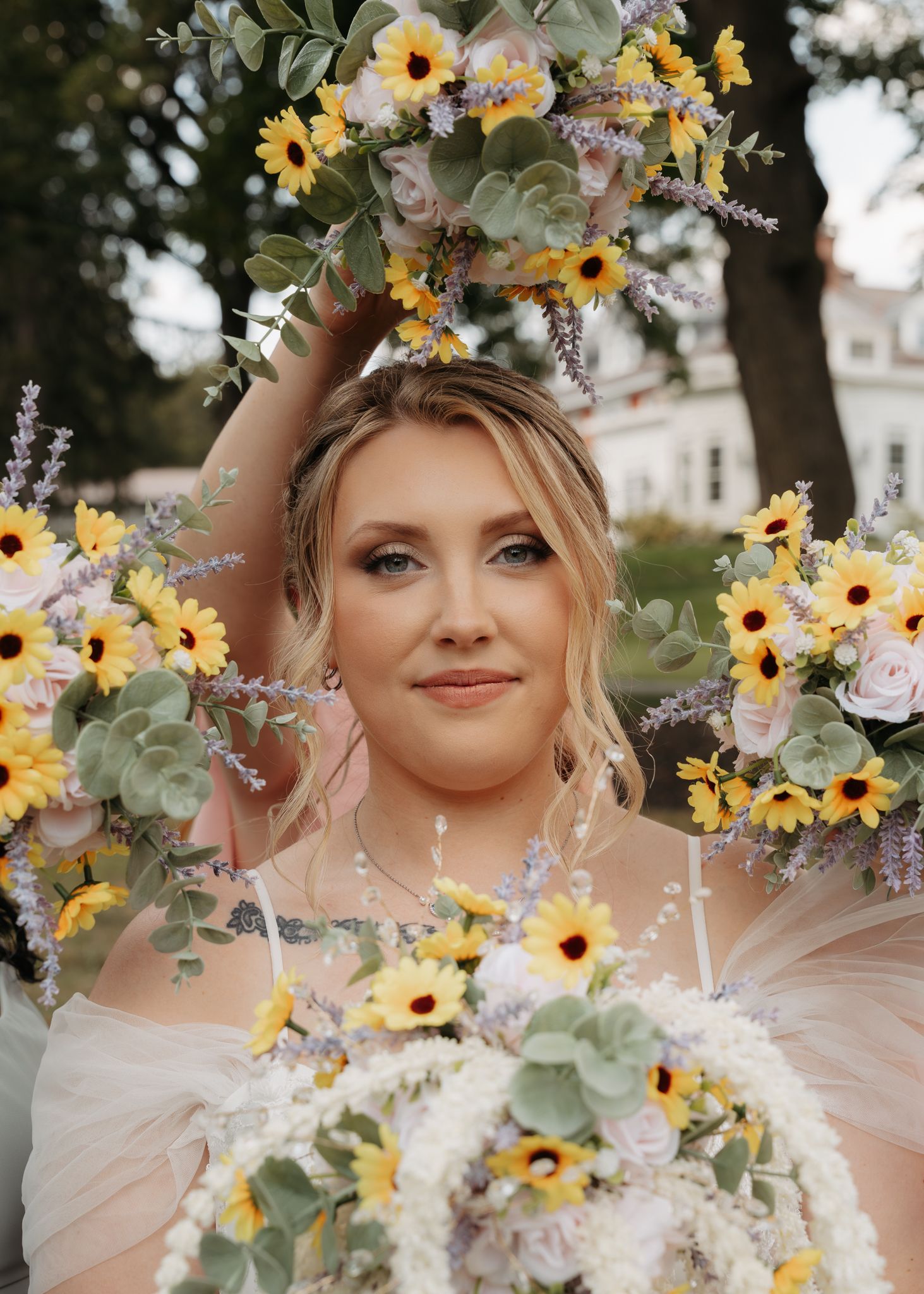 Bride surrounded by sunflower and lavender bouquets smiling at outdoor wedding photo session.