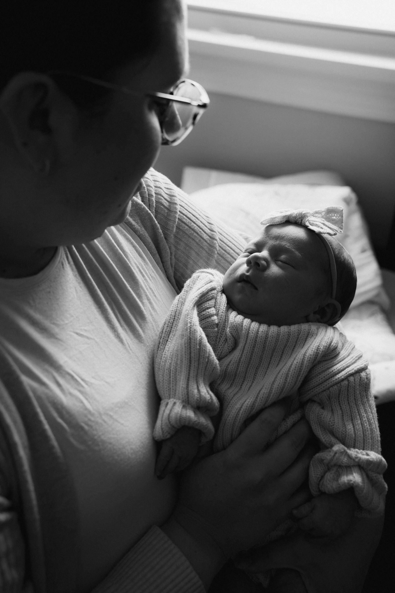Black and white photo of parent tenderly holding sleeping newborn baby indoors.