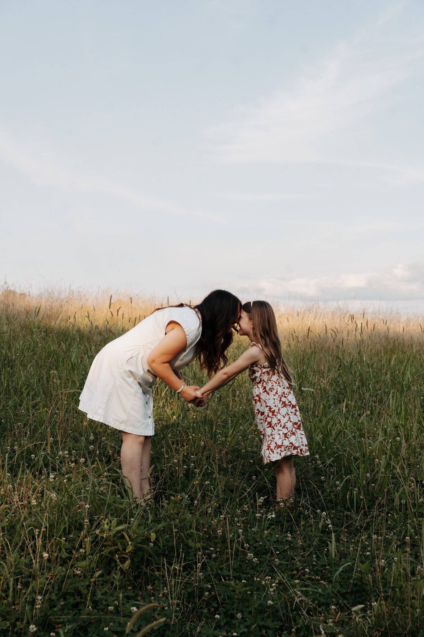 Mother and young daughter sharing a tender nose kiss in a tall grass meadow.
