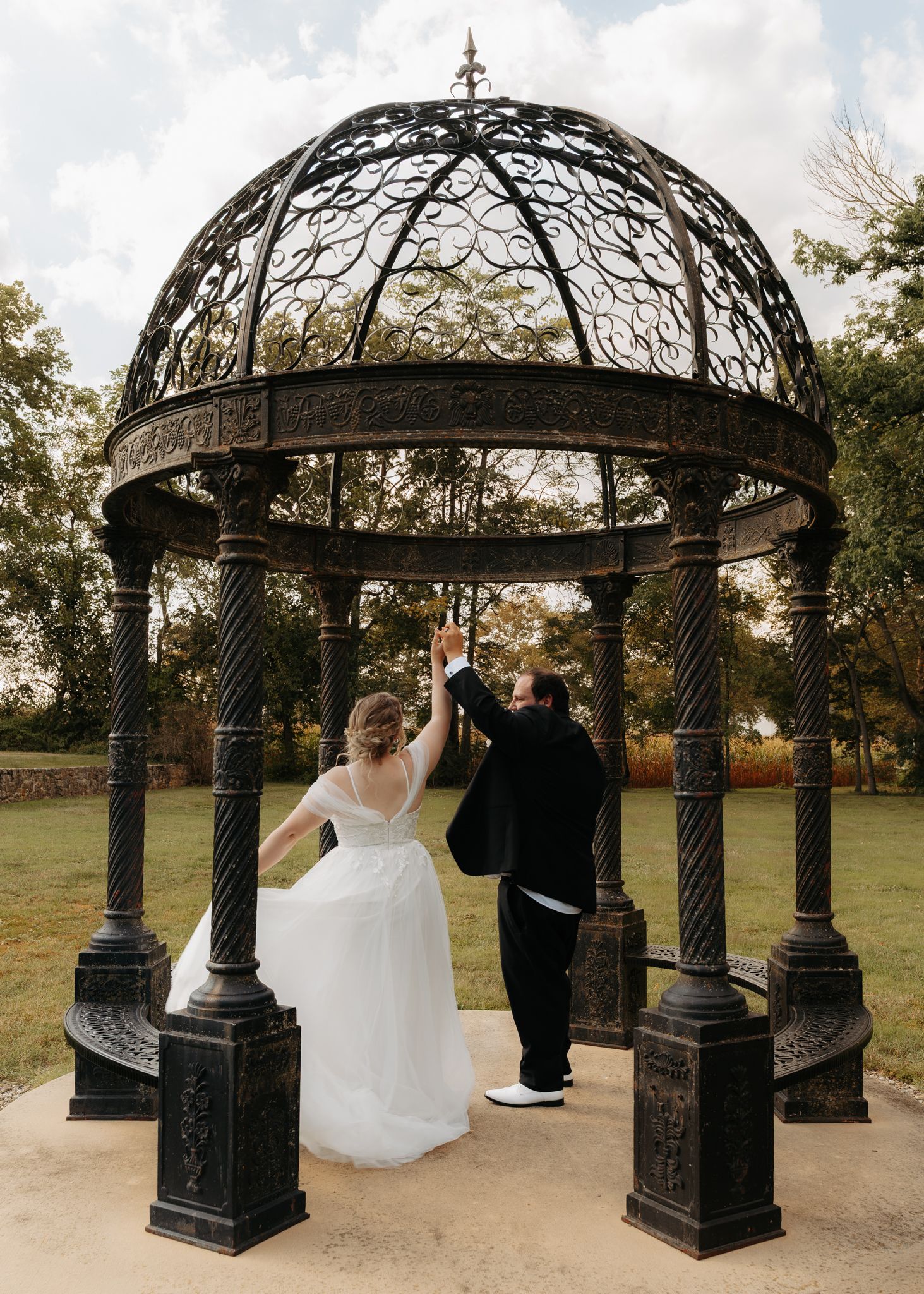 Bride and groom dancing under an ornate black iron gazebo dome at outdoor wedding venue.