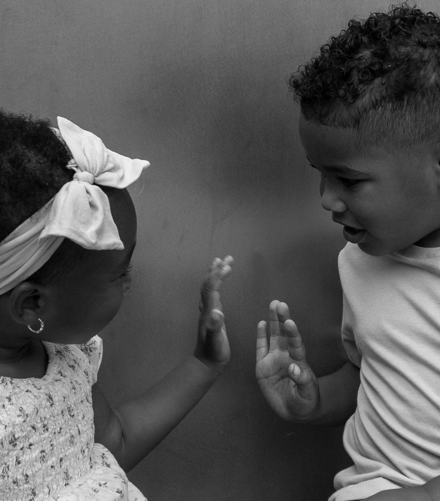 Black and white photo of two young children facing each other with hands raised, appearing to play together.
