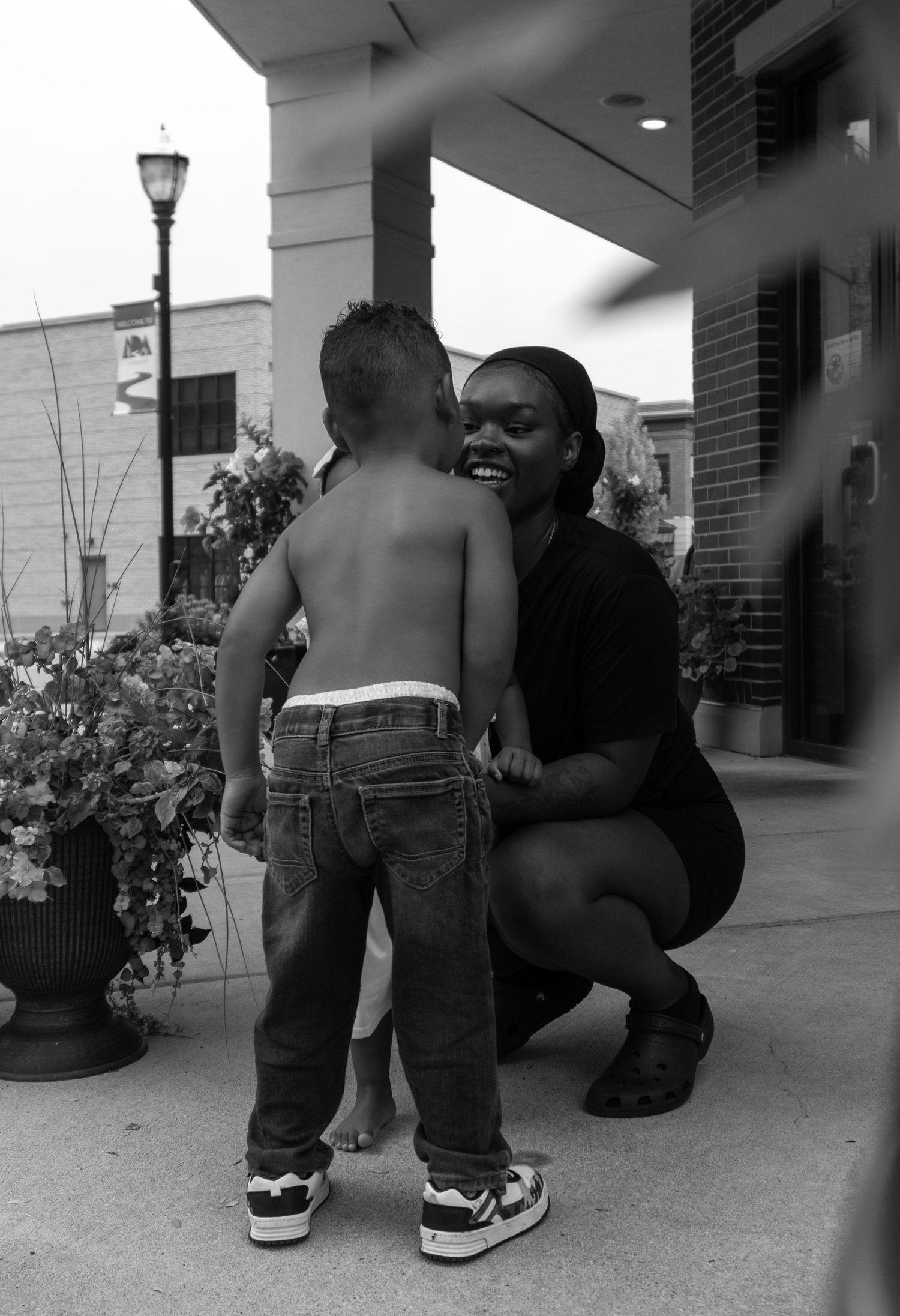 Black and white photo of young woman crouching and smiling with toddler boy outdoors.
