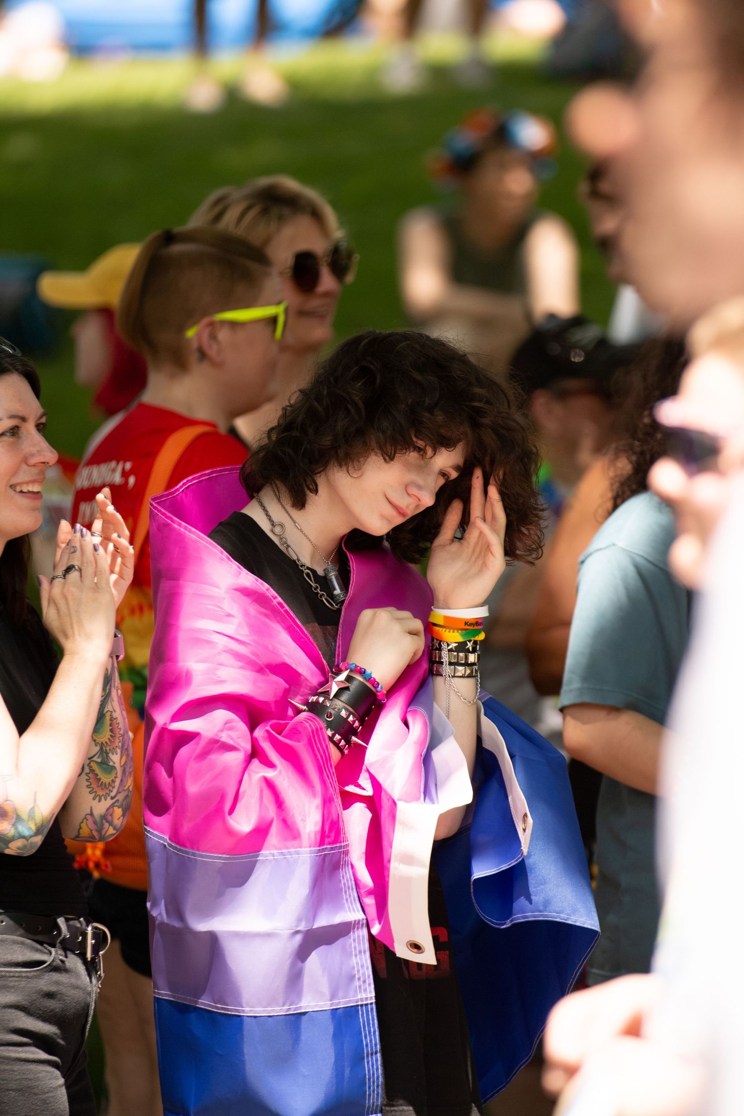 A person wearing a Bisexual flag, playing with their hair in a crowd of people.