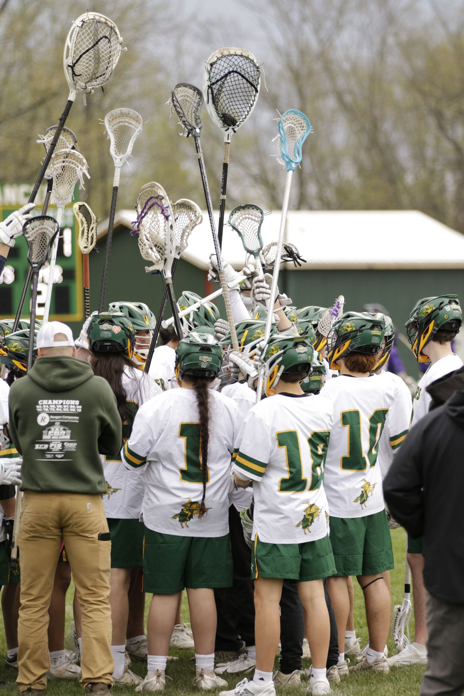 A group of lacrosse players holding up their lacrosse sticks and cheering for one another in a circle.