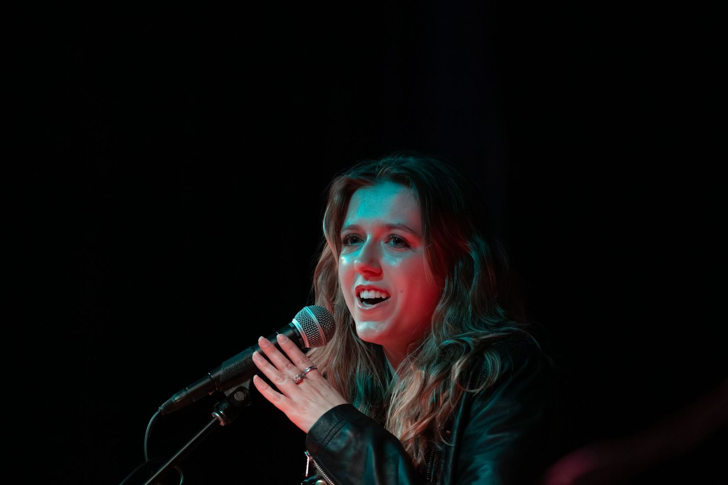 A person happily singing into a microphone, slightly holding onto it.