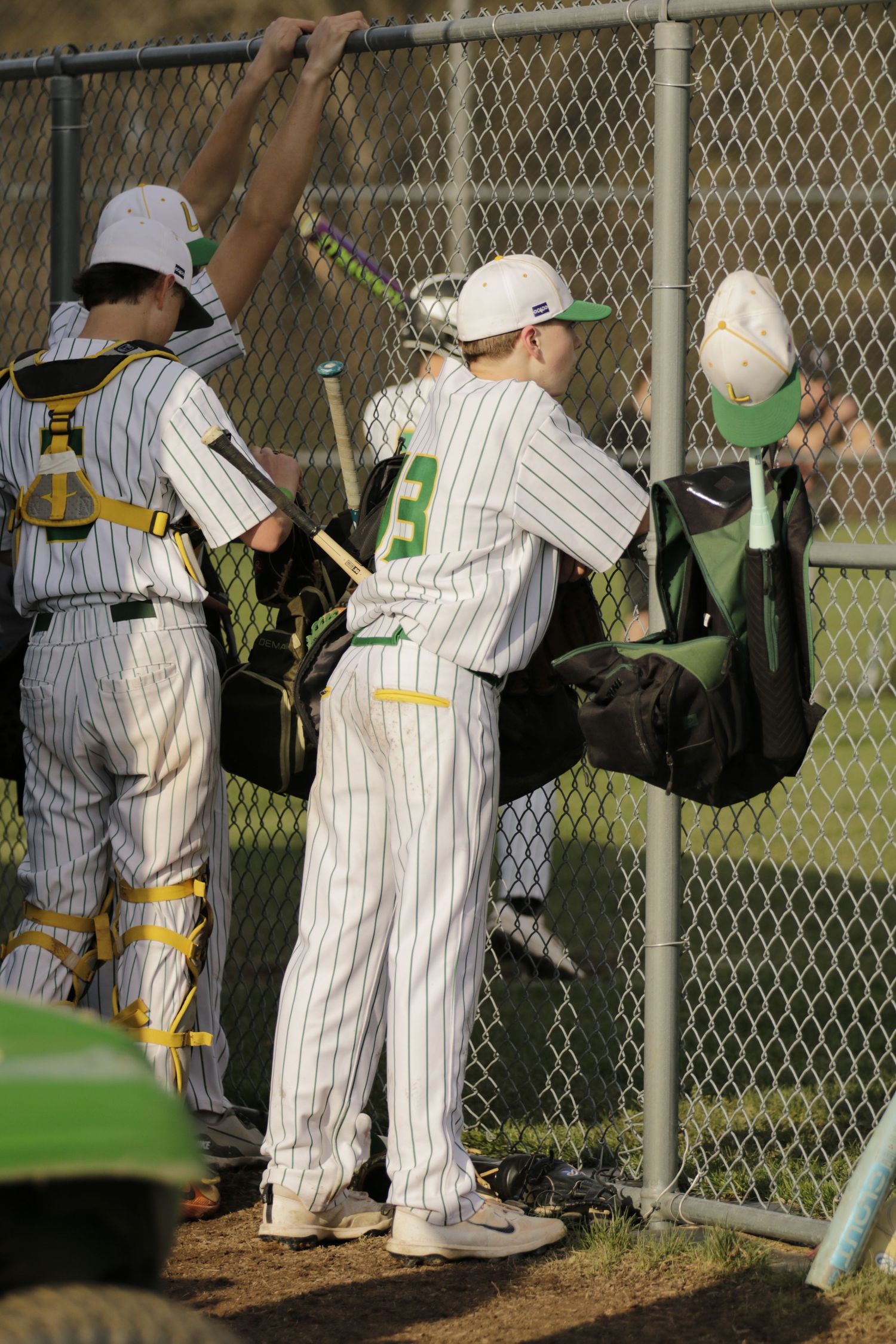 A baseball player leaning on a fence with a ray of sunlight hitting them.
