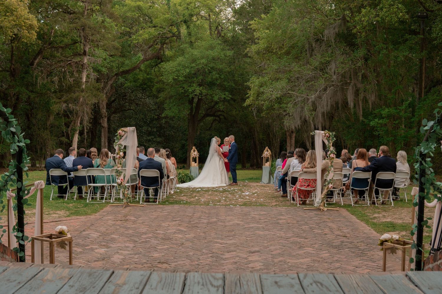 Outdoor rustic woodland wedding ceremony with brick aisle and wooden arch in forest setting.