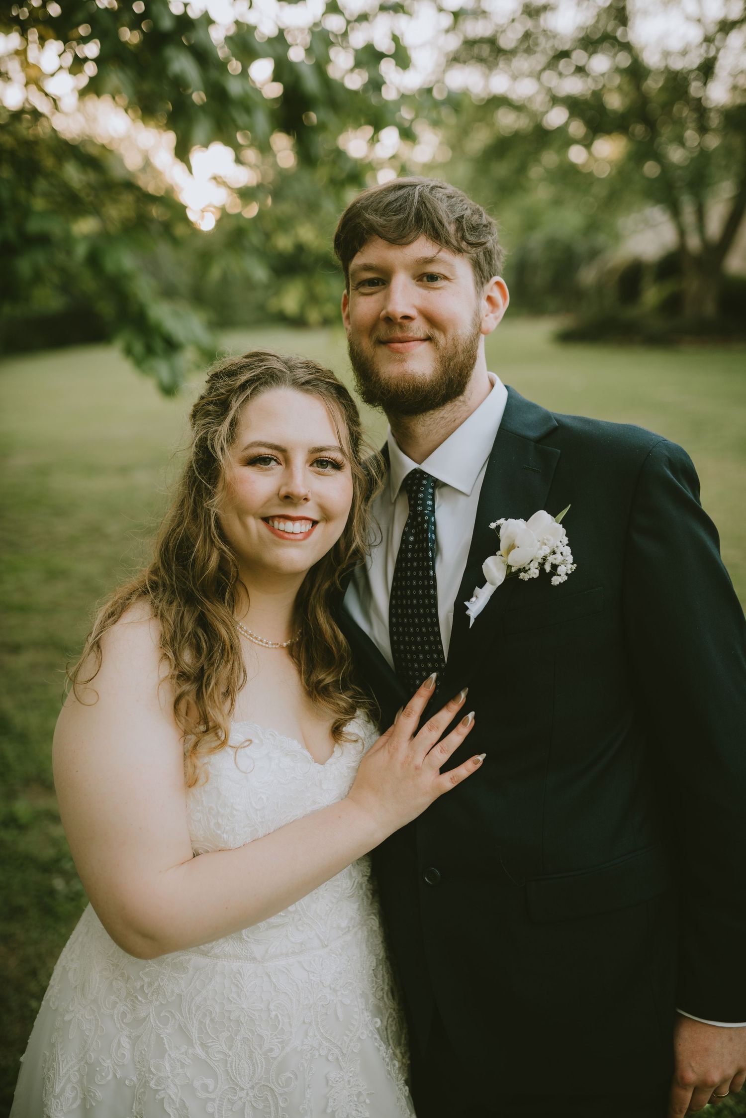 A smiling bride and groom pose together outdoors in a lush green garden setting on their wedding day.