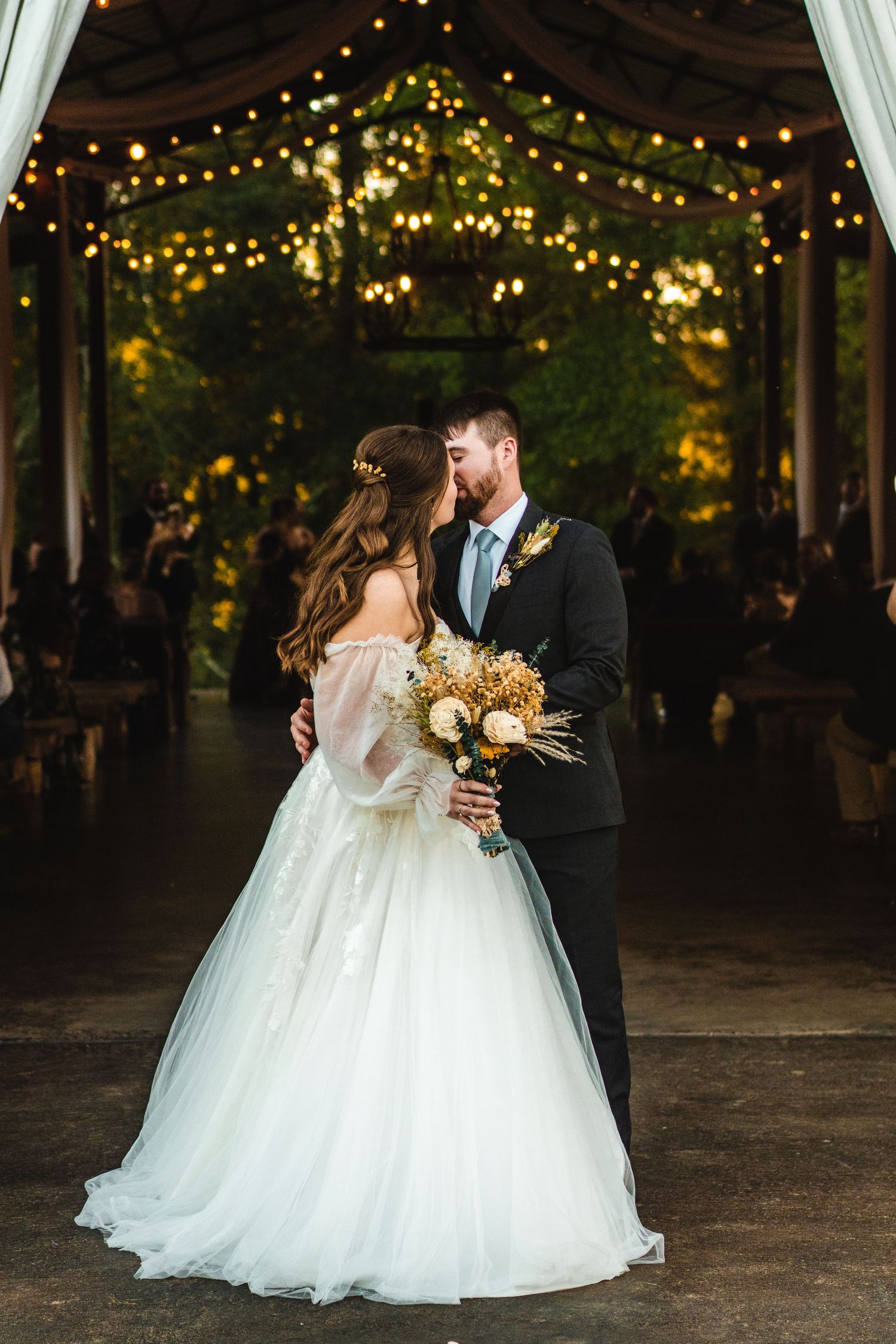 Bride and groom share romantic moment under string lights at elegant outdoor wedding venue.