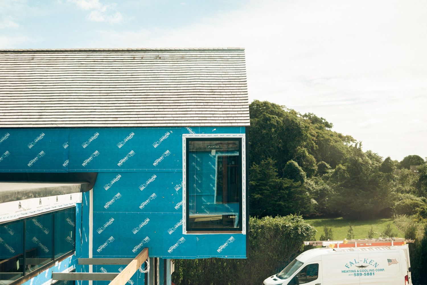 New home construction with blue Tyvek weather barrier and slate roof with a work van nearby.