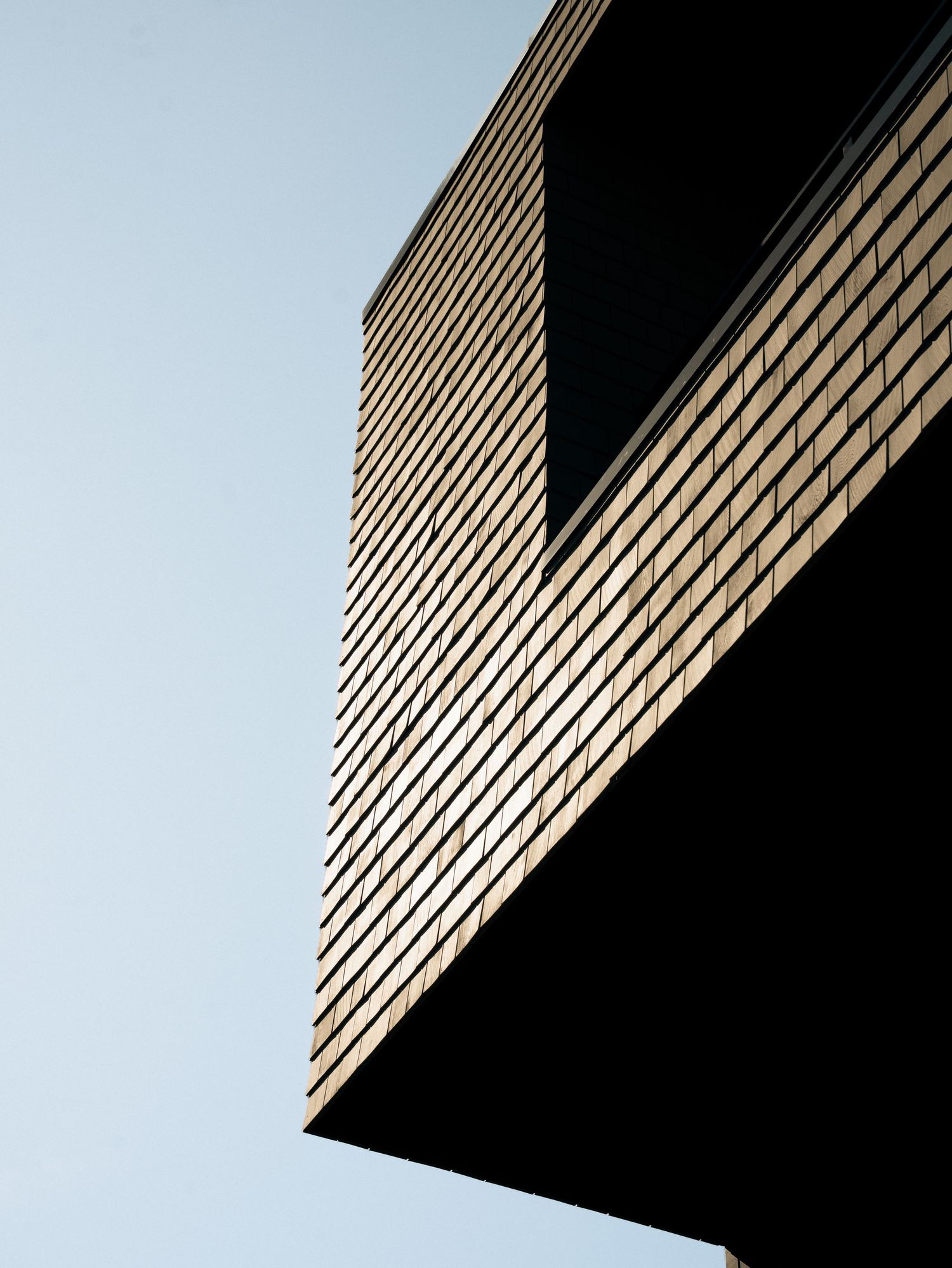 Low-angle view of a modern building corner with wooden slat cladding against a clear blue sky.