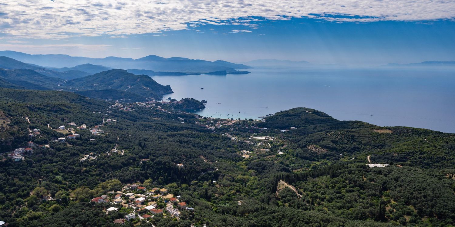 Aerial panoramic view of lush green coastline with blue sea and scattered buildings. Photo Taken by AJCoatesPhotography