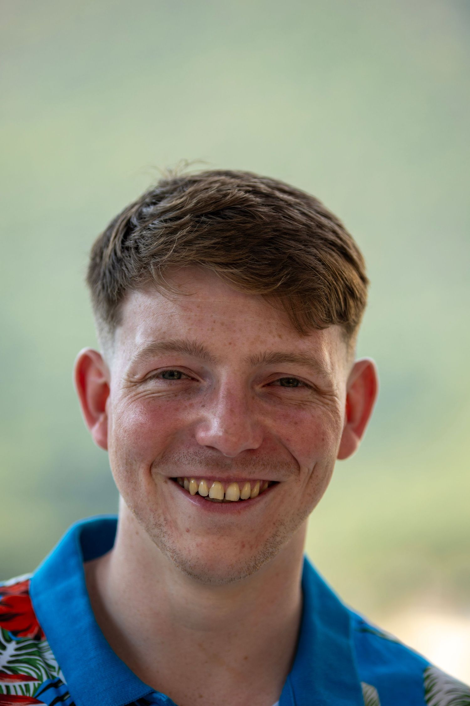 Smiling young man with freckles wearing blue floral shirt outdoors. Photo Taken by AJCoatesPhotography