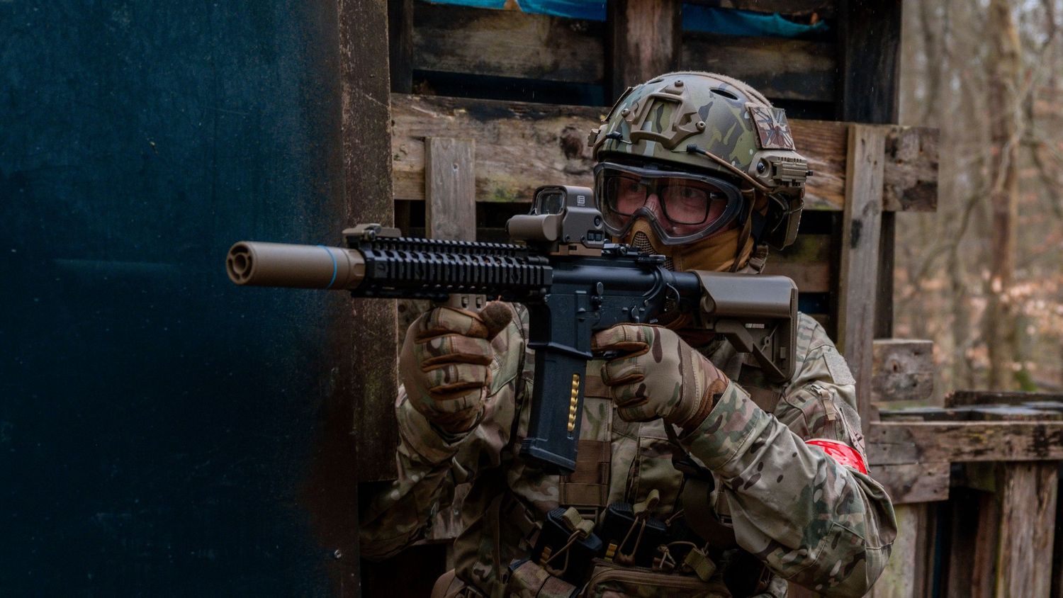 Soldier in multicam uniform aiming rifle from wooden structure during outdoor tactical training. Photo Taken by AJCoatesPhotography