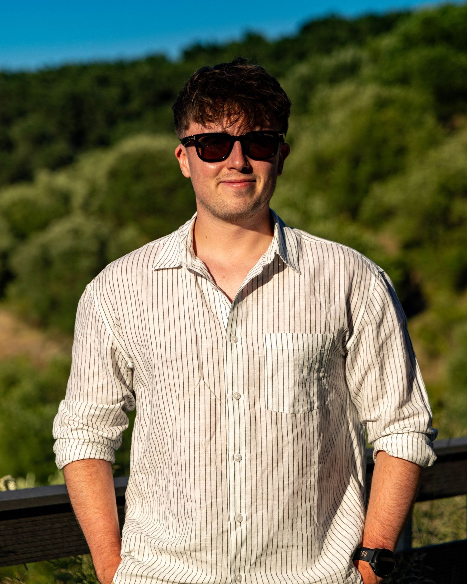 Young man wearing striped shirt and sunglasses standing outdoors in sunny nature. Photo Taken by AJCoatesPhotography