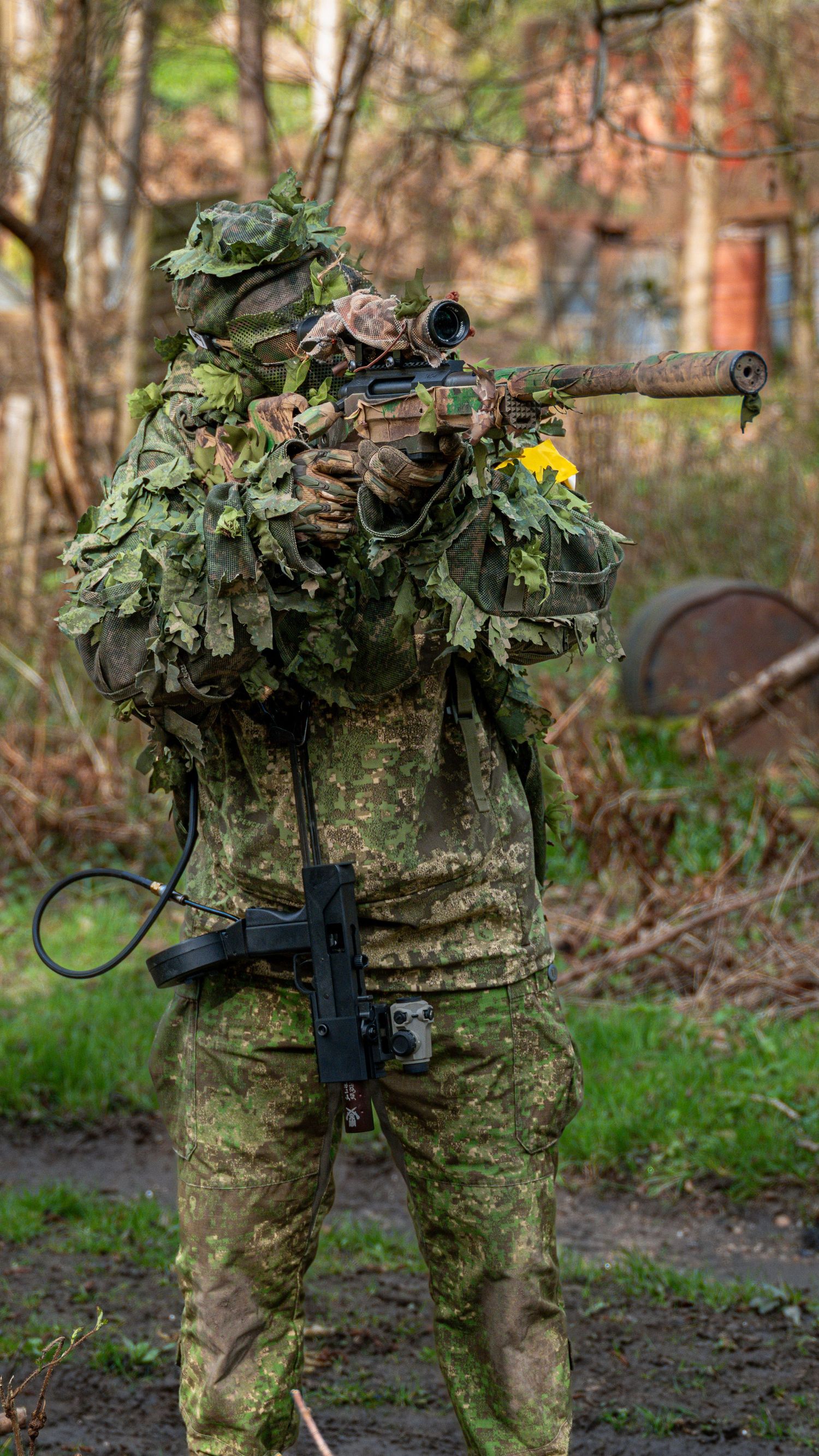 Camouflaged sniper in ghillie suit aiming rifle in outdoor woodland setting. Photo Taken by AJCoatesPhotography
