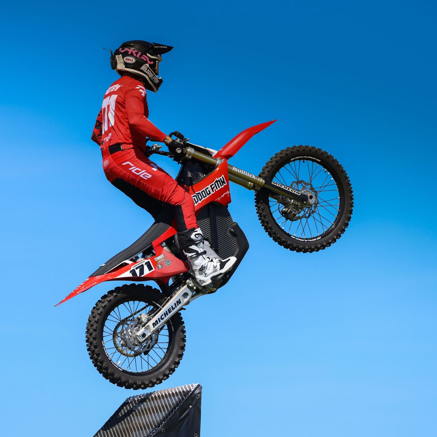 Motocross rider in red gear launching off a ramp on a red dirt bike numbered 171 against blue sky. Photo Taken by AJCoatesPhotography