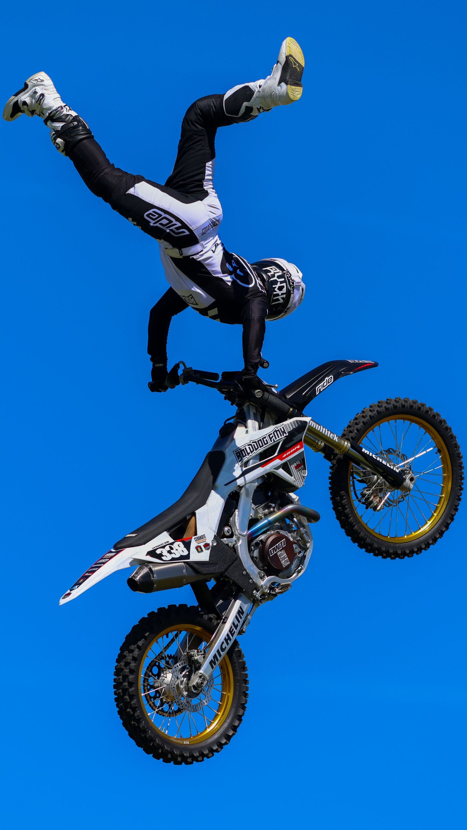 Freestyle motocross rider performs an inverted trick on a dirt bike against a vivid blue sky. Photo Taken by AJCoatesPhotography