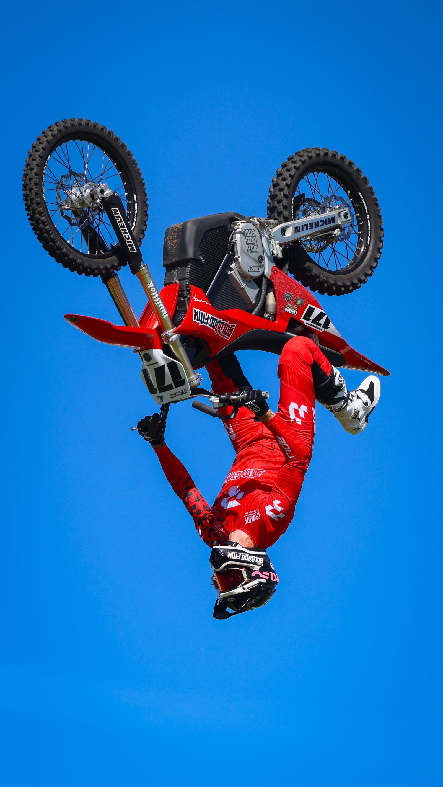 FMX rider in red gear performing an inverted aerial trick on a dirt bike against blue sky. Photo Taken by AJCoatesPhotography