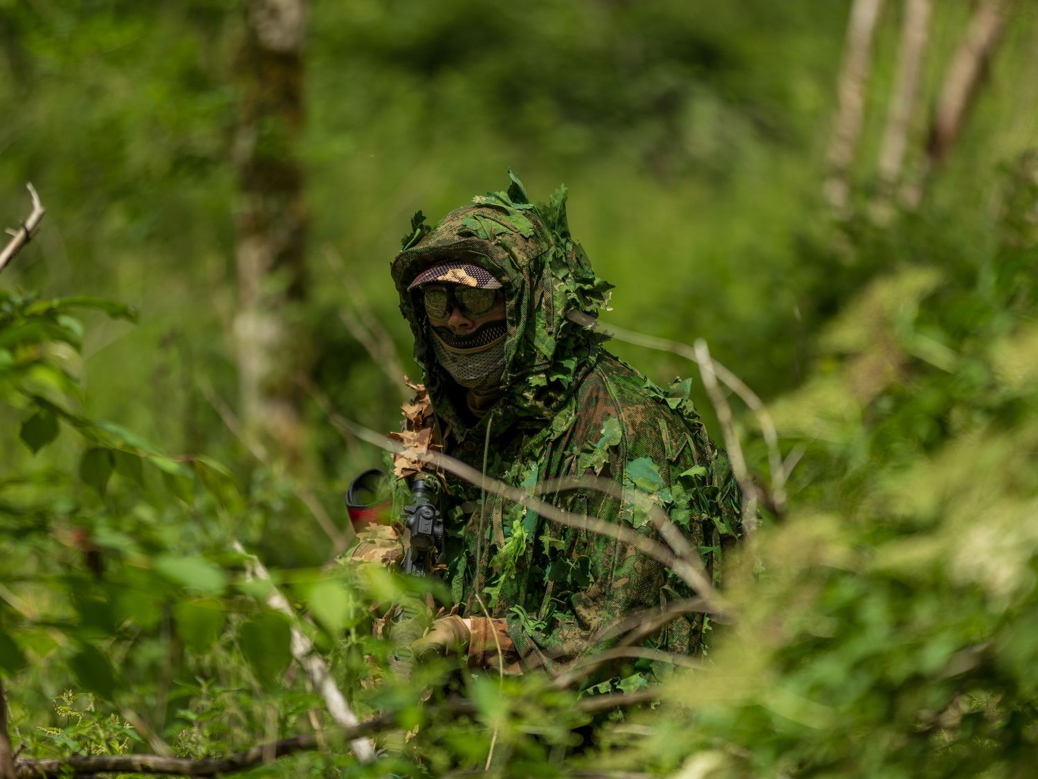 Sniper in green ghillie suit concealed among dense forest foliage during outdoor military training exercise. Photo Taken by AJCoatesPhotogra