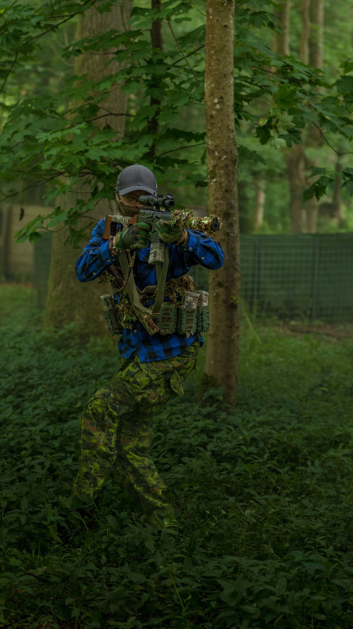Airsoft player in camouflage gear aiming rifle in dense green forest during tactical game. Photo Taken by AJCoatesPhotography