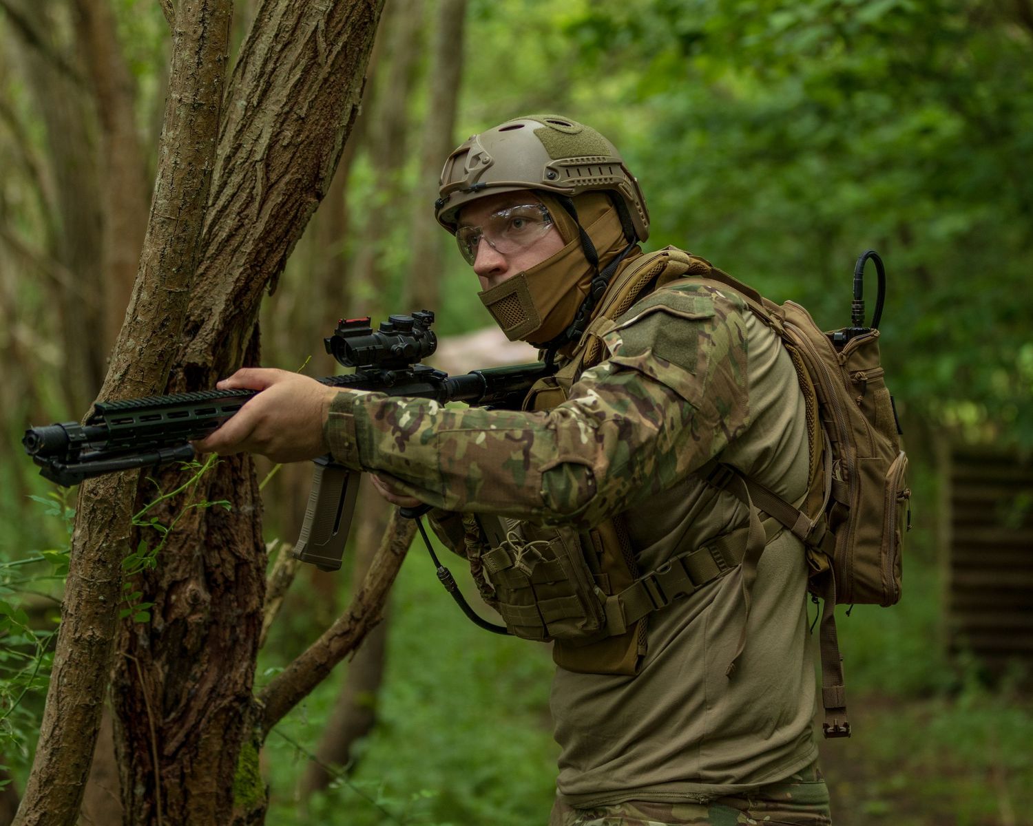 Soldier in camouflage gear aiming rifle behind tree in forest during military training exercise. Photo Taken by AJCoatesPhotography
