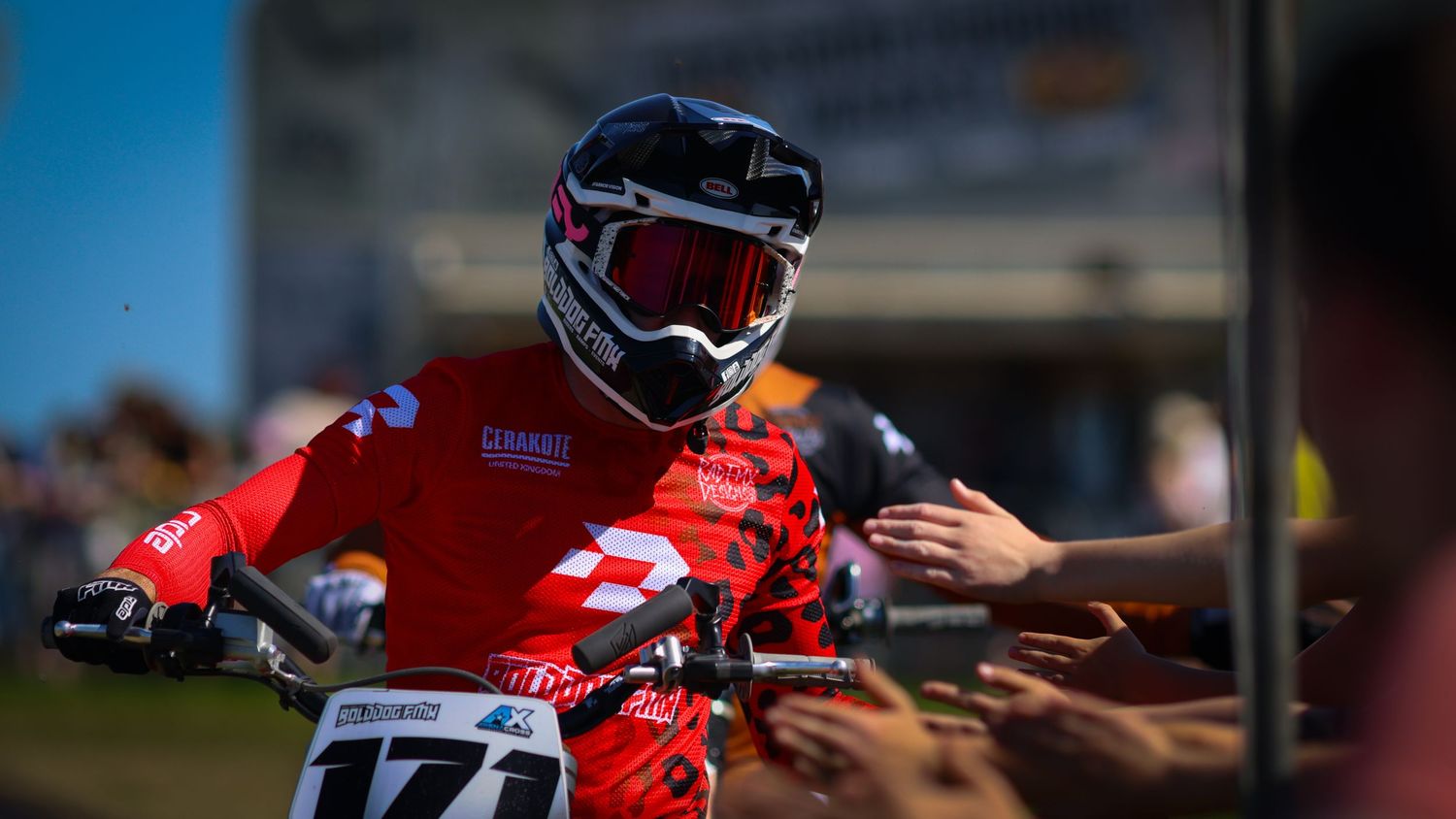 Motocross rider in red gear greeting fans while on dirt bike numbered 171 at a sunny event. Photo Taken by AJCoatesPhotography