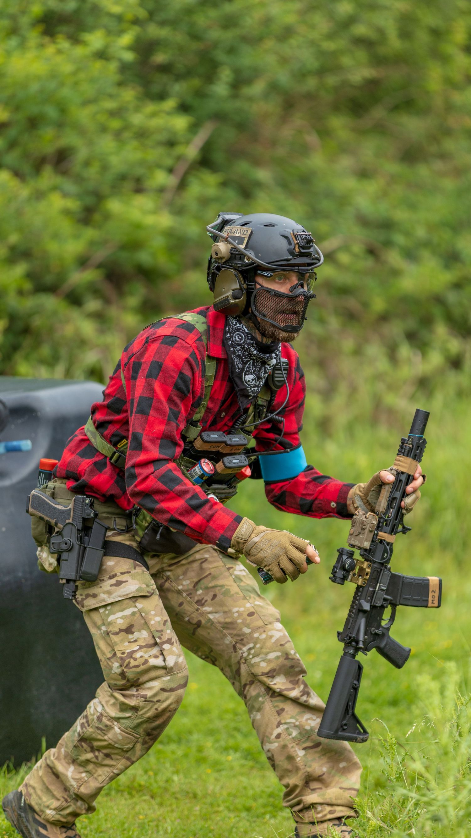 Airsoft player in red plaid shirt and tactical helmet running with assault rifle on grass field. Photo Taken by AJCoatesPhotography