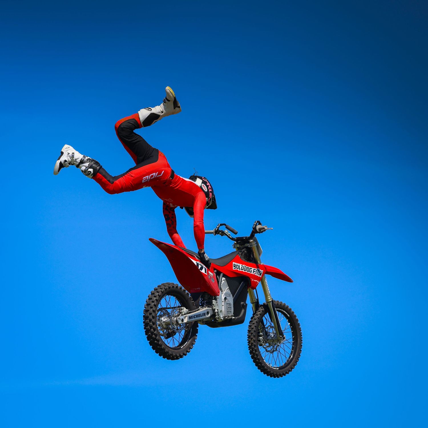 Freestyle motocross athlete in red gear performing a trick on a red dirt bike mid-air. Photo Taken by AJCoatesPhotography