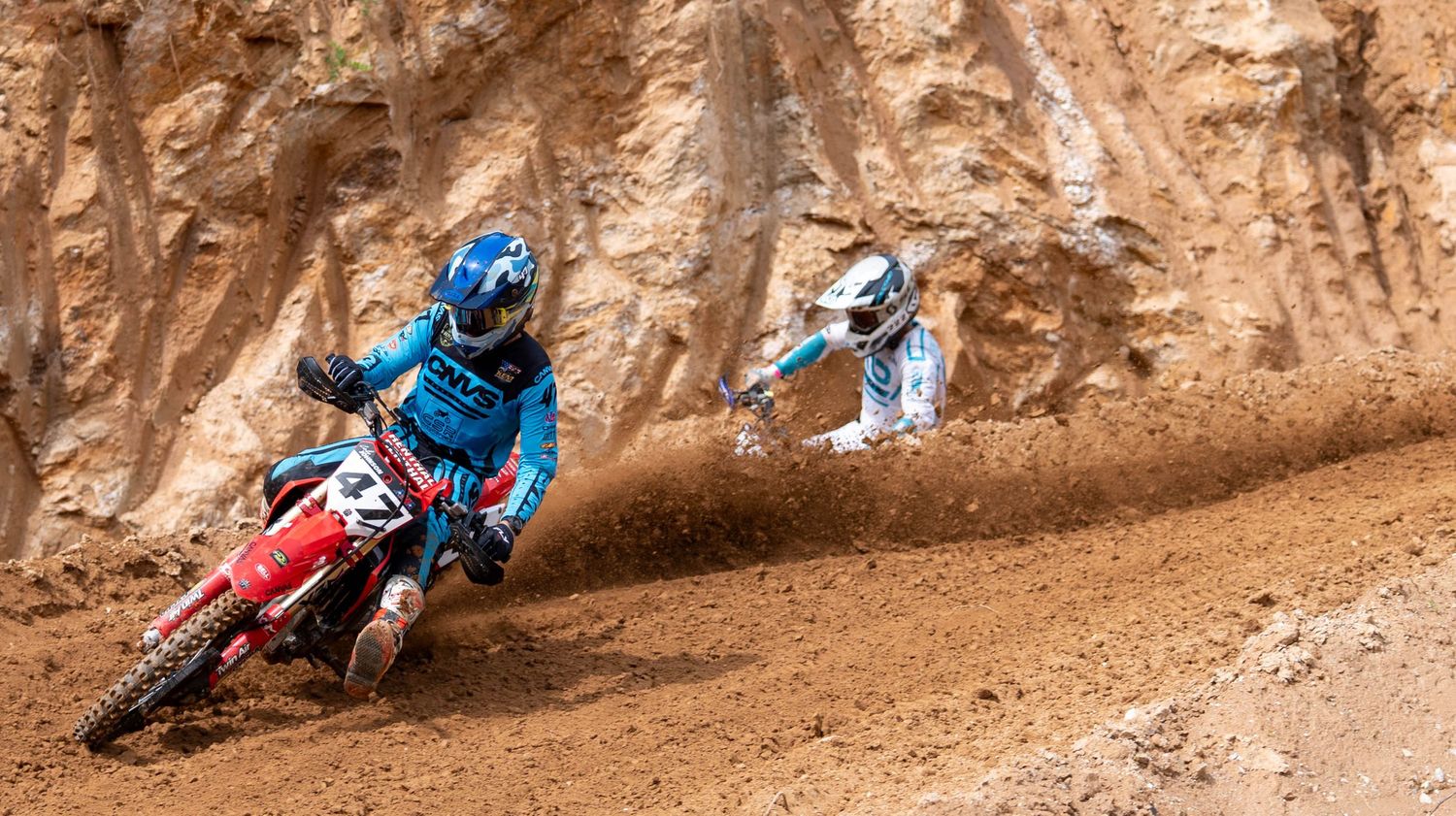 Two motocross riders racing through a steep dirt berm.