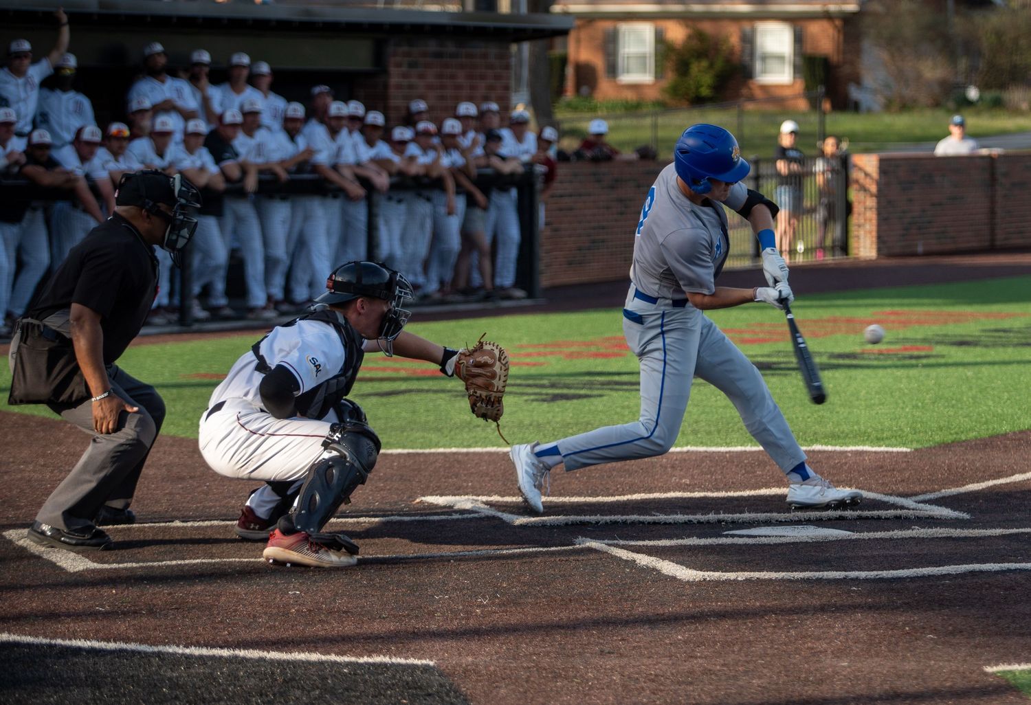 Baseball player swings at a pitch as the catcher and umpire watch at home plate.