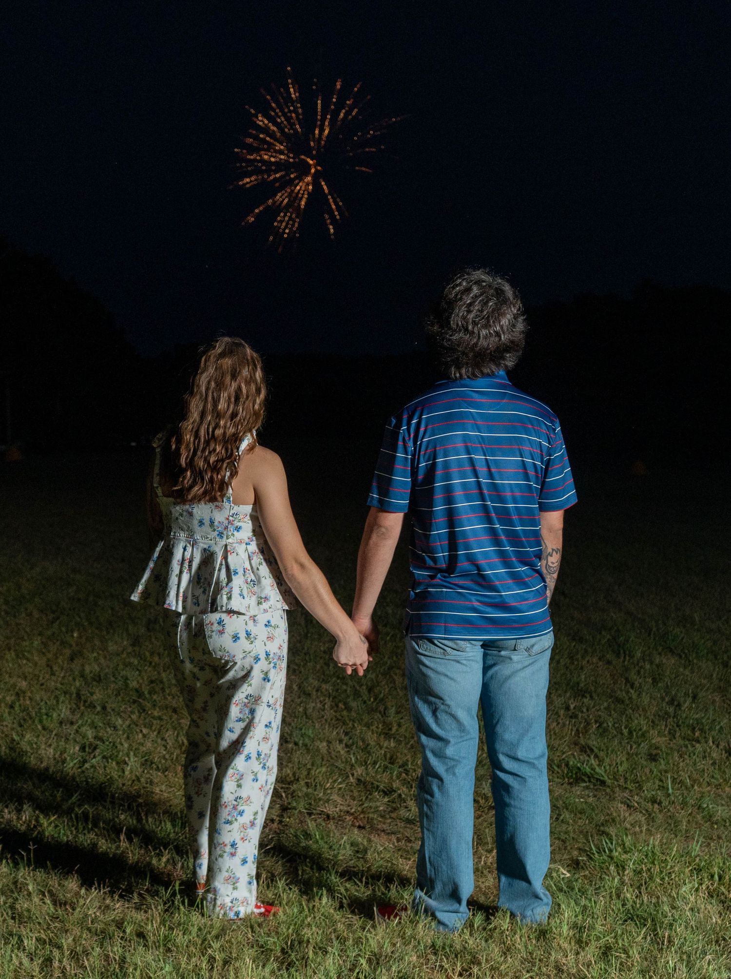 Couple holding hands while watching fireworks at night.