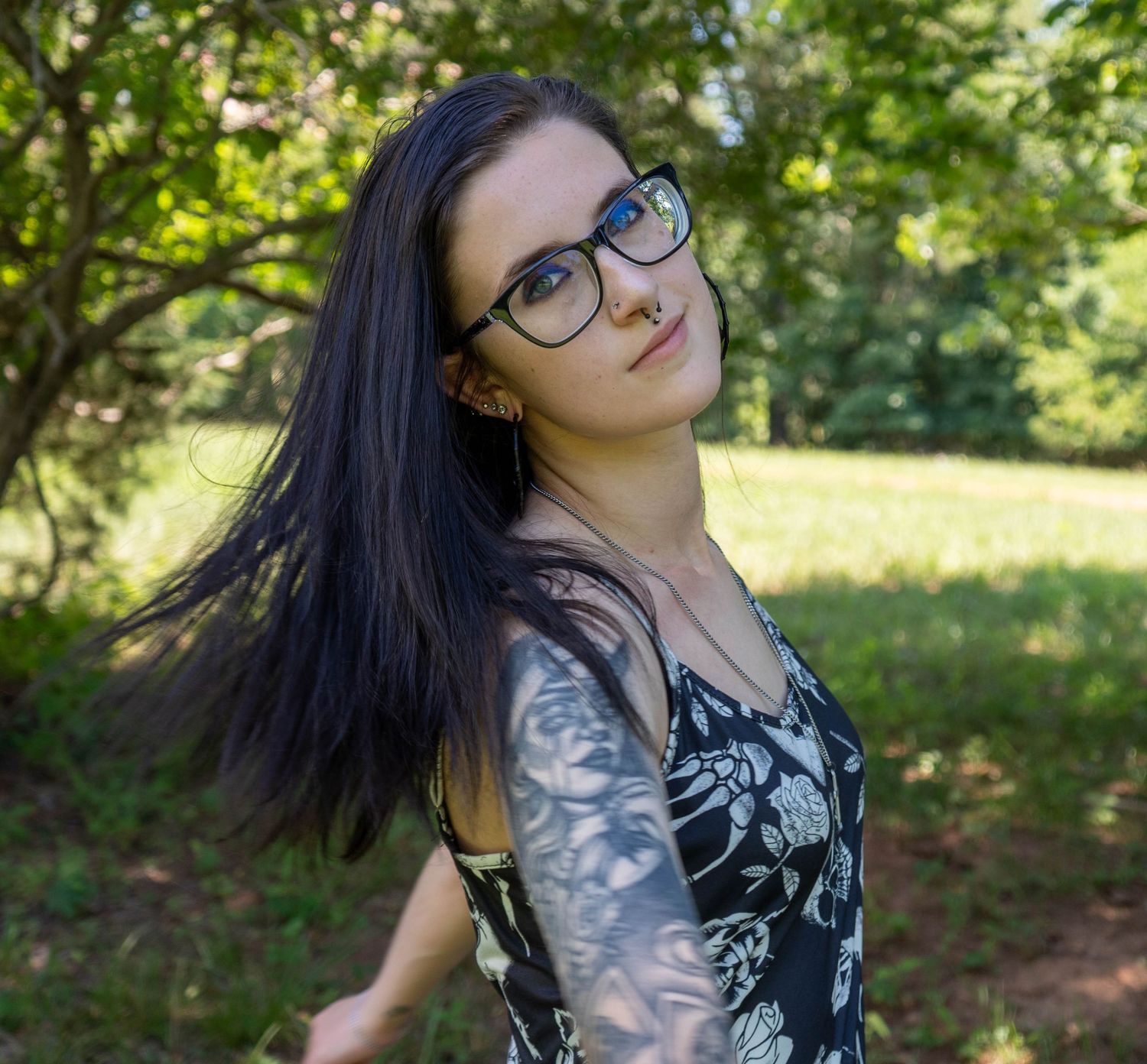 Outdoor portrait of a woman with dark hair and glasses in a wooded setting.