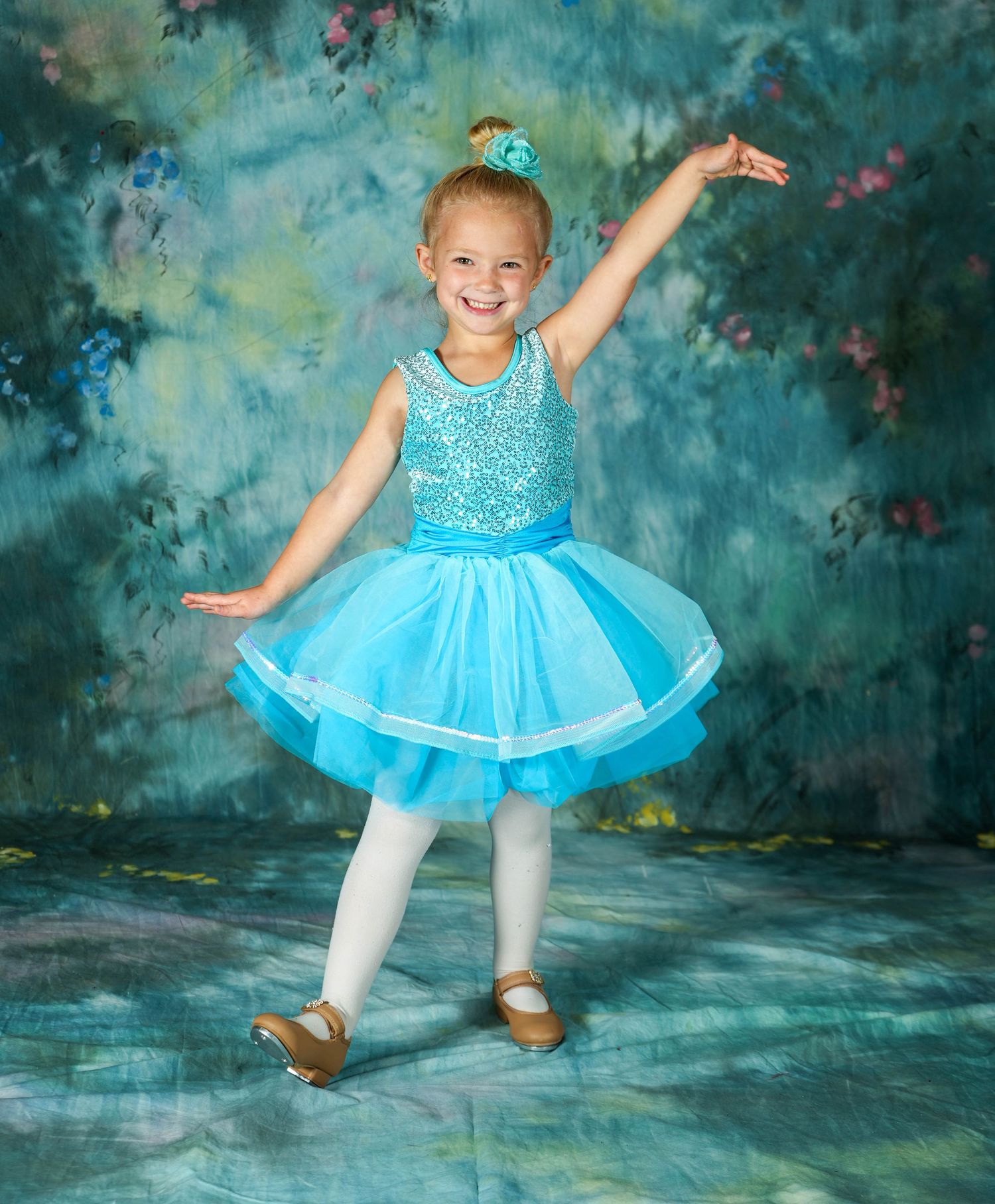 Young ballerina posing in a blue tutu against a blue studio backdrop.