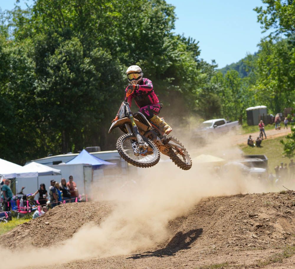 Motocross rider jumping over a dirt mound with dust trailing behind.