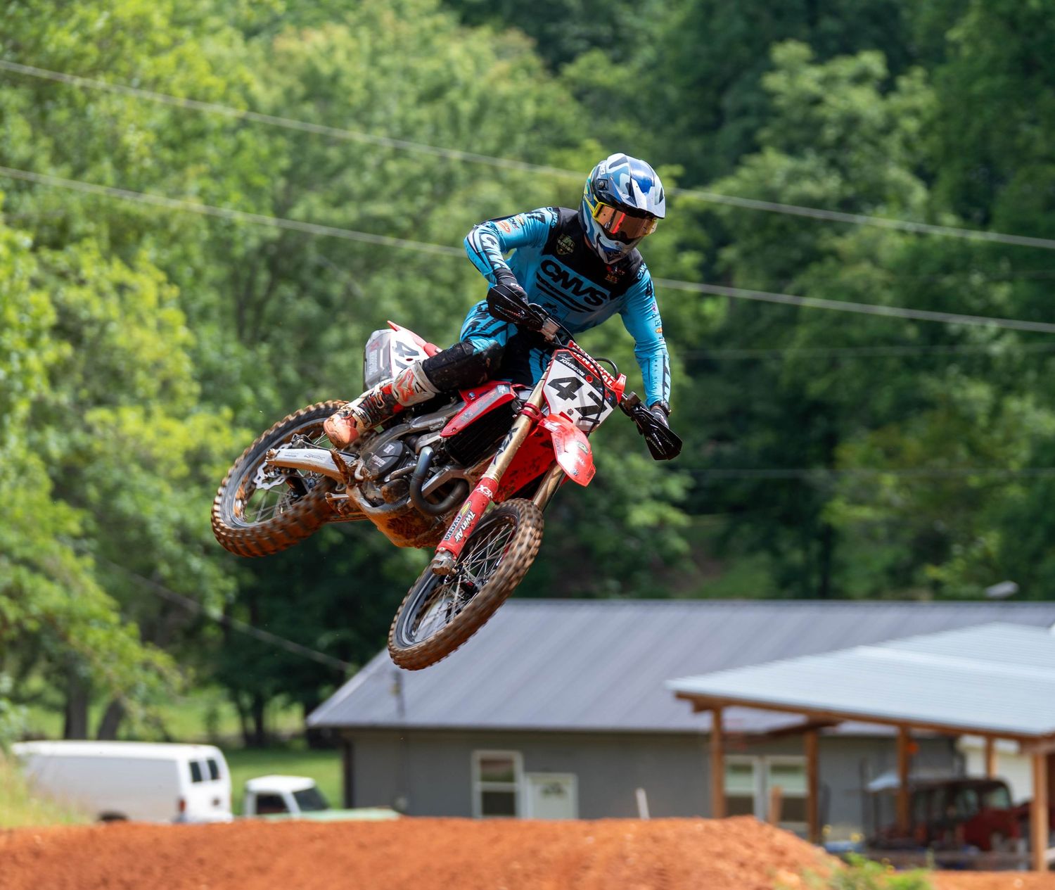 Motocross rider airborne over a jump on a red dirt track.