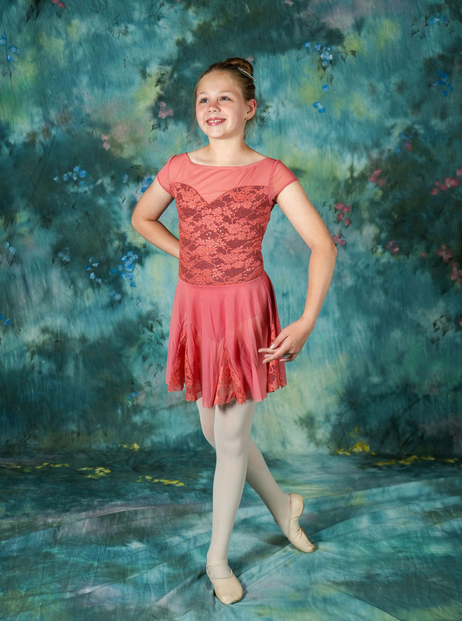 Young dancer posing in a coral dance costume against a blue studio backdrop.