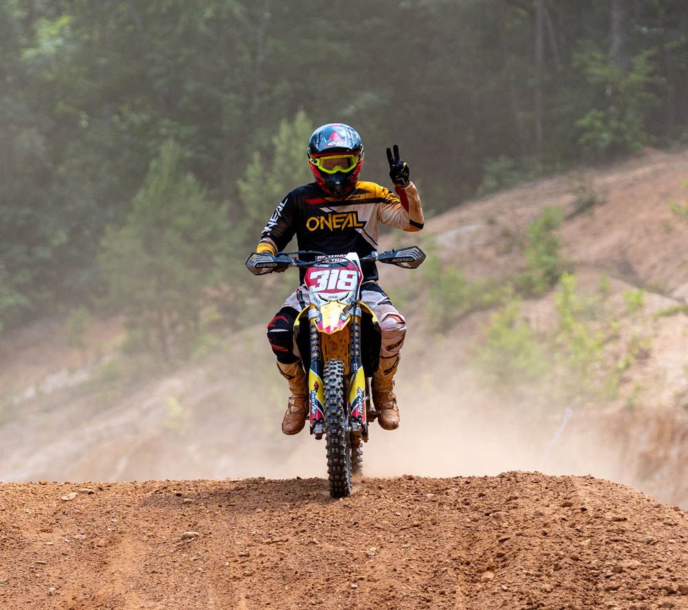 Motocross rider approaching over a dirt rise with dust behind them.