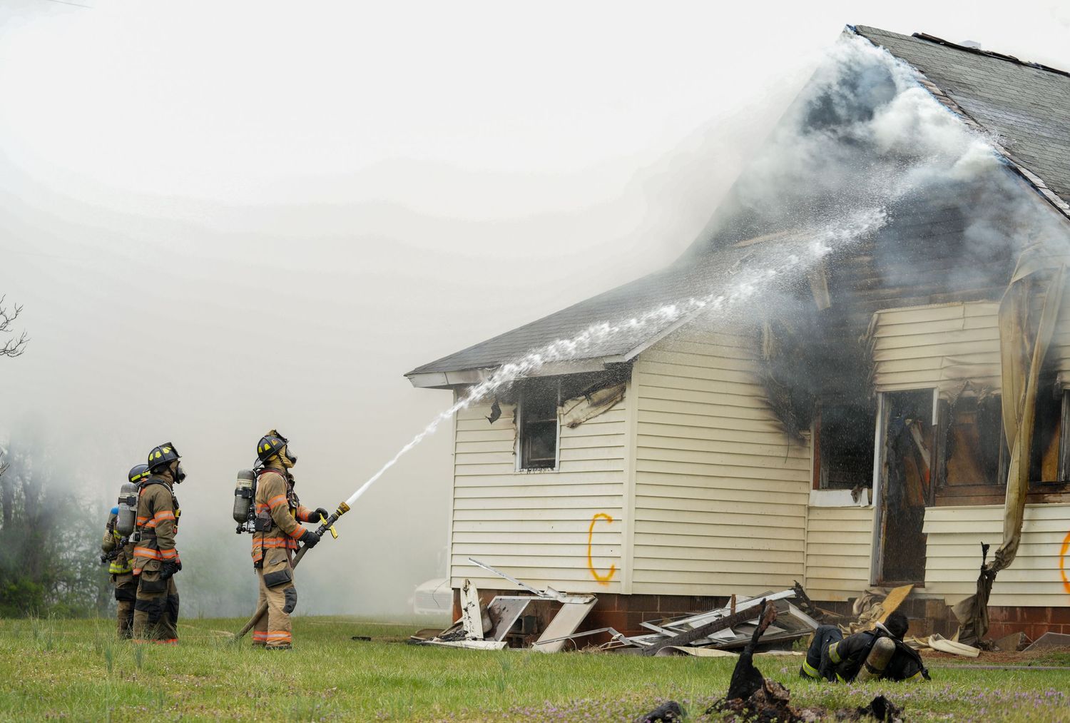 Firefighters spray water onto the roof of a smoke-filled house during a training exercise.
