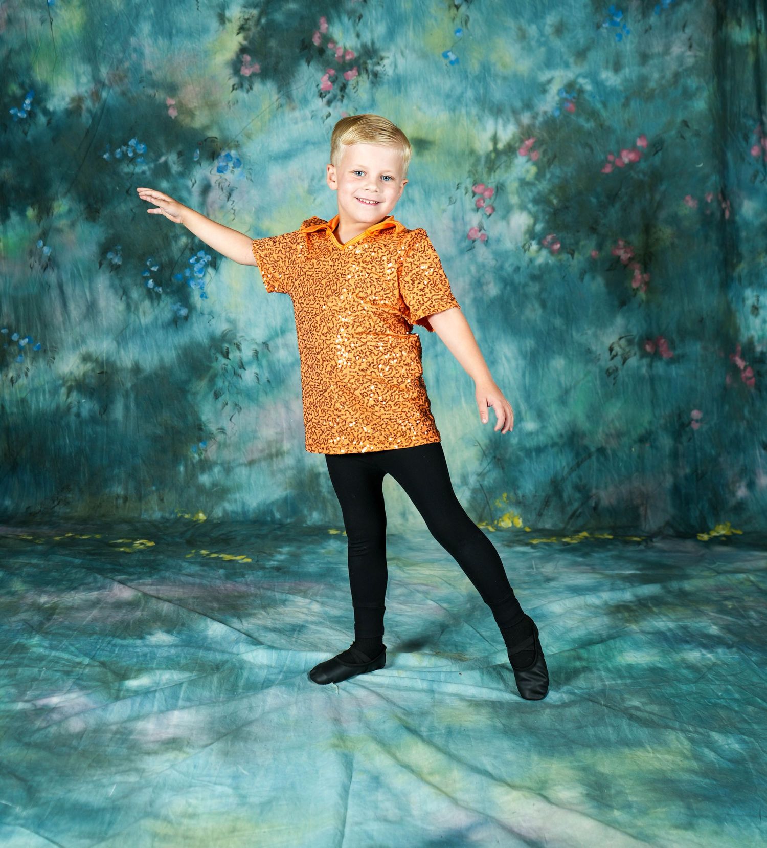 Young dancer posing in an orange costume against a blue studio backdrop.