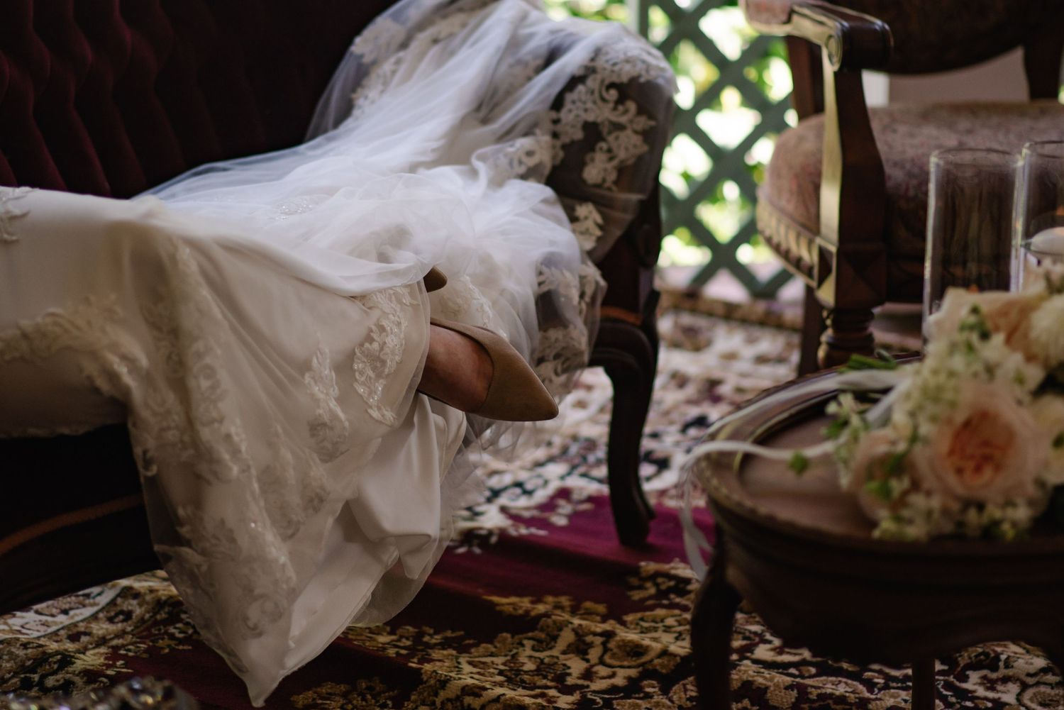 A flowing white wedding dress train with delicate lace details trails across a wooden floor.