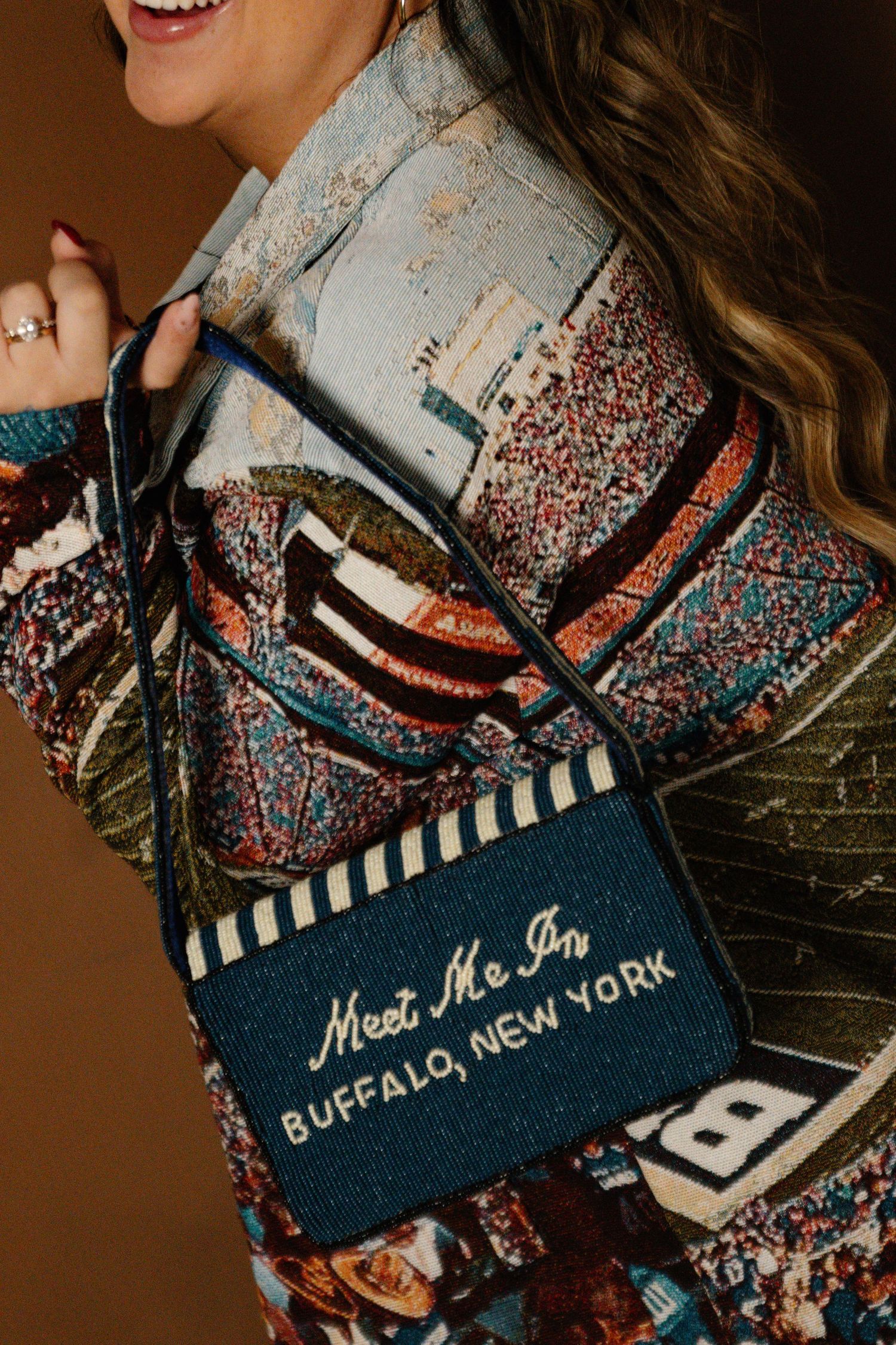 Woman carrying a navy blue beaded crossbody bag embroidered with Meet Me In Buffalo, New York.