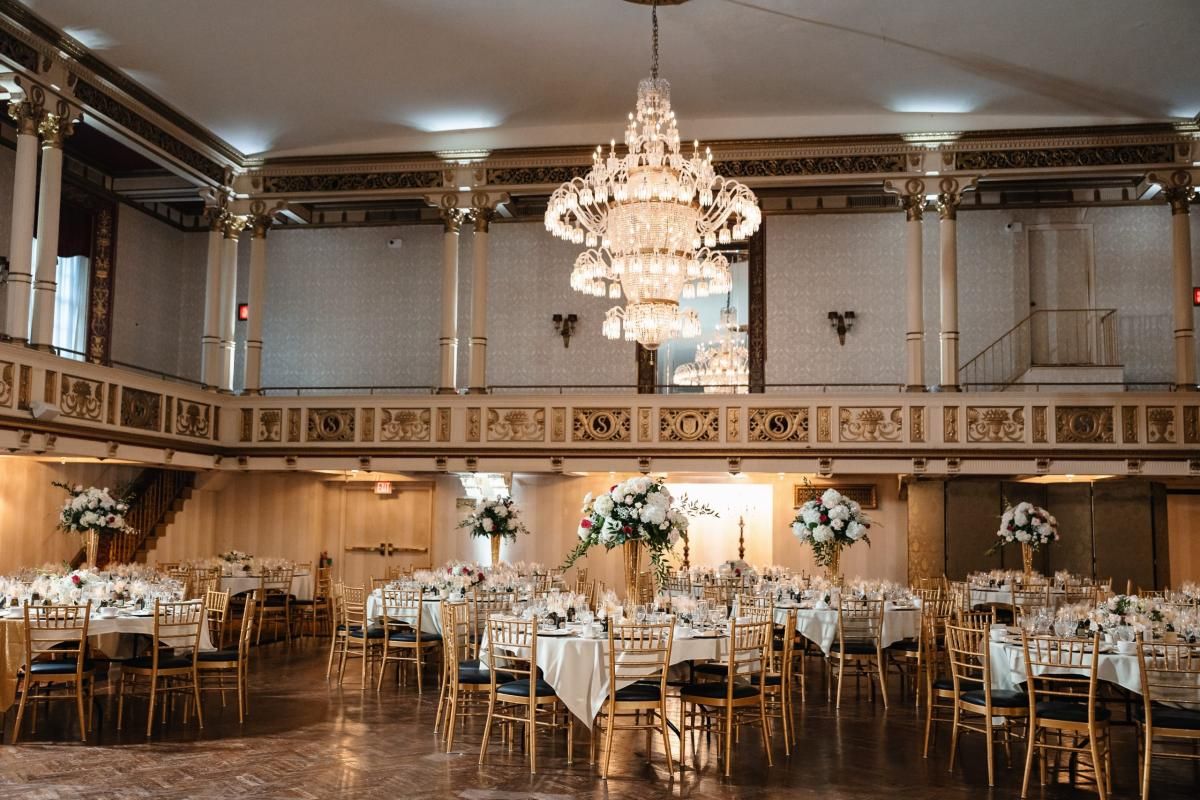 Elegant ballroom with crystal chandeliers, white tables, and gold chairs set for a luxurious wedding reception.