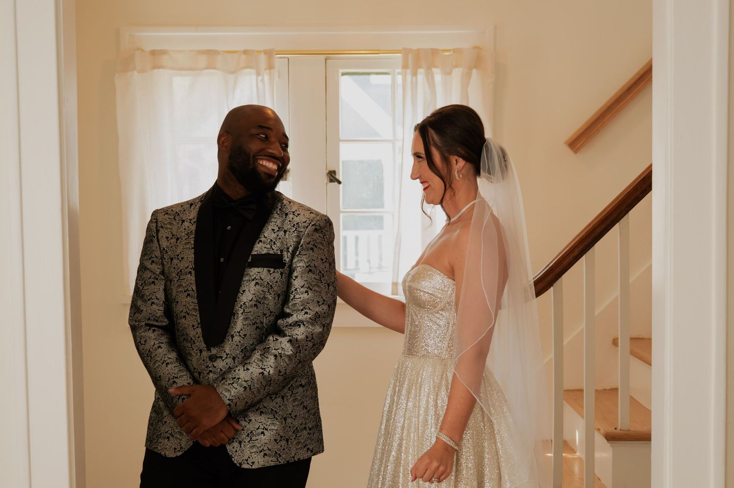 A couple shares a joyful first look moment before their wedding, with the bride in white and groom in patterned jacket.