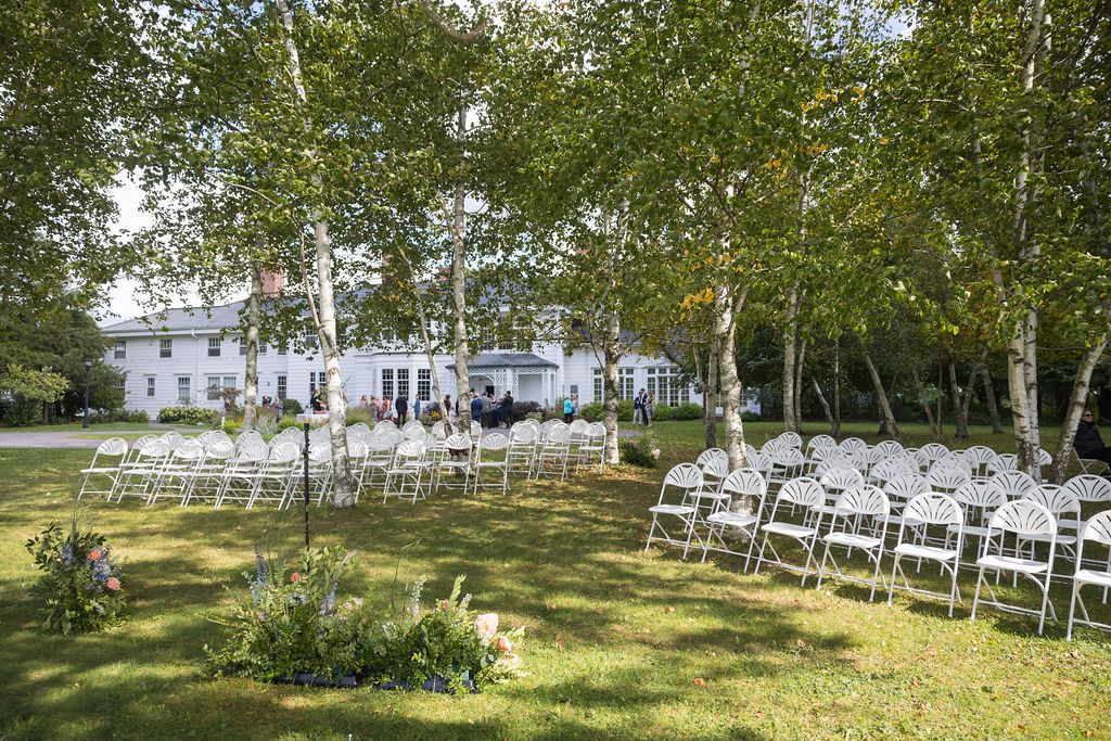 White chairs arranged in rows for an outdoor wedding ceremony under tall birch trees in a natural setting.