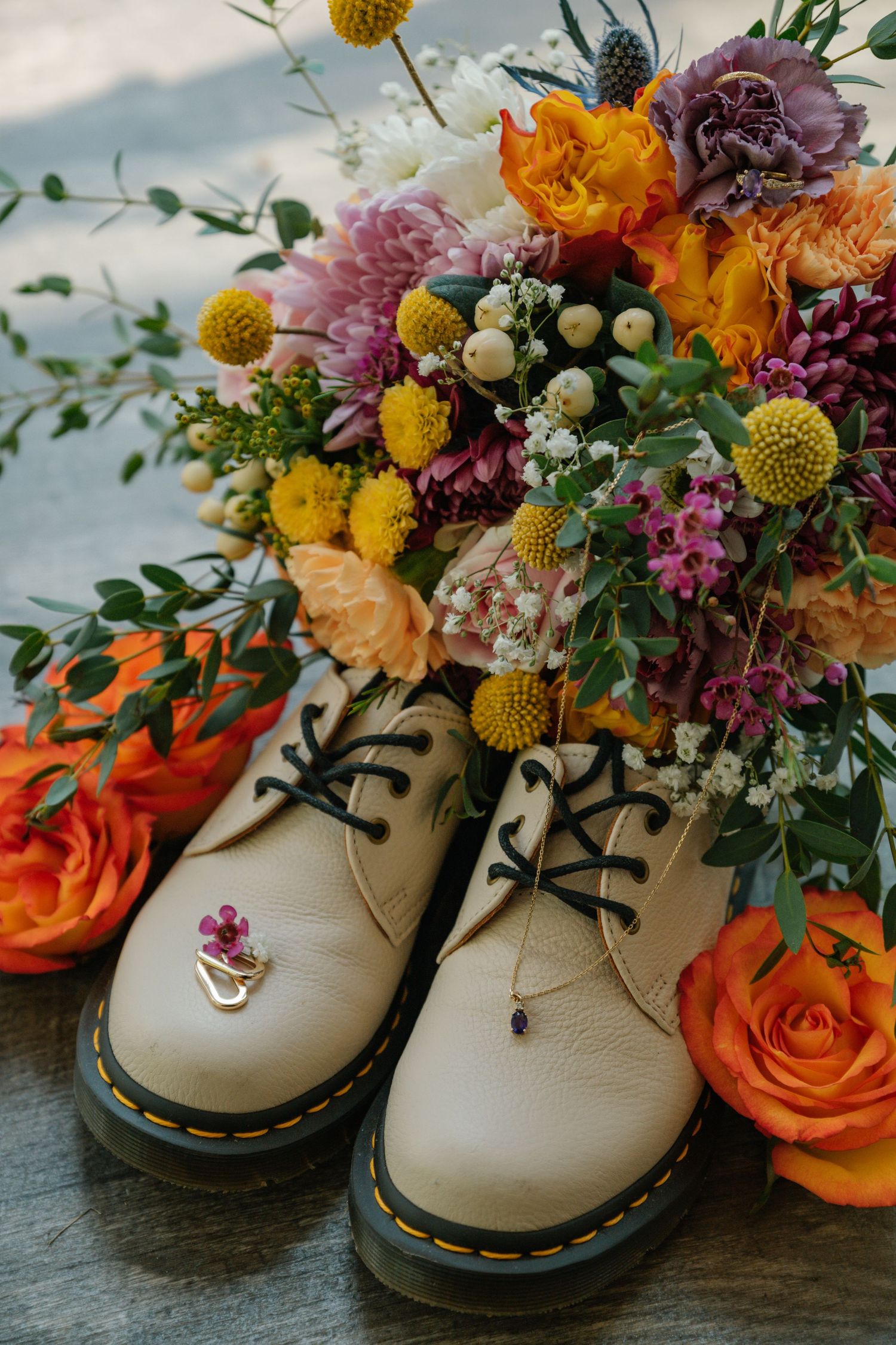 White leather boots filled with vibrant orange roses, purple stock flowers, and yellow craspedia create a whimsical floral display.